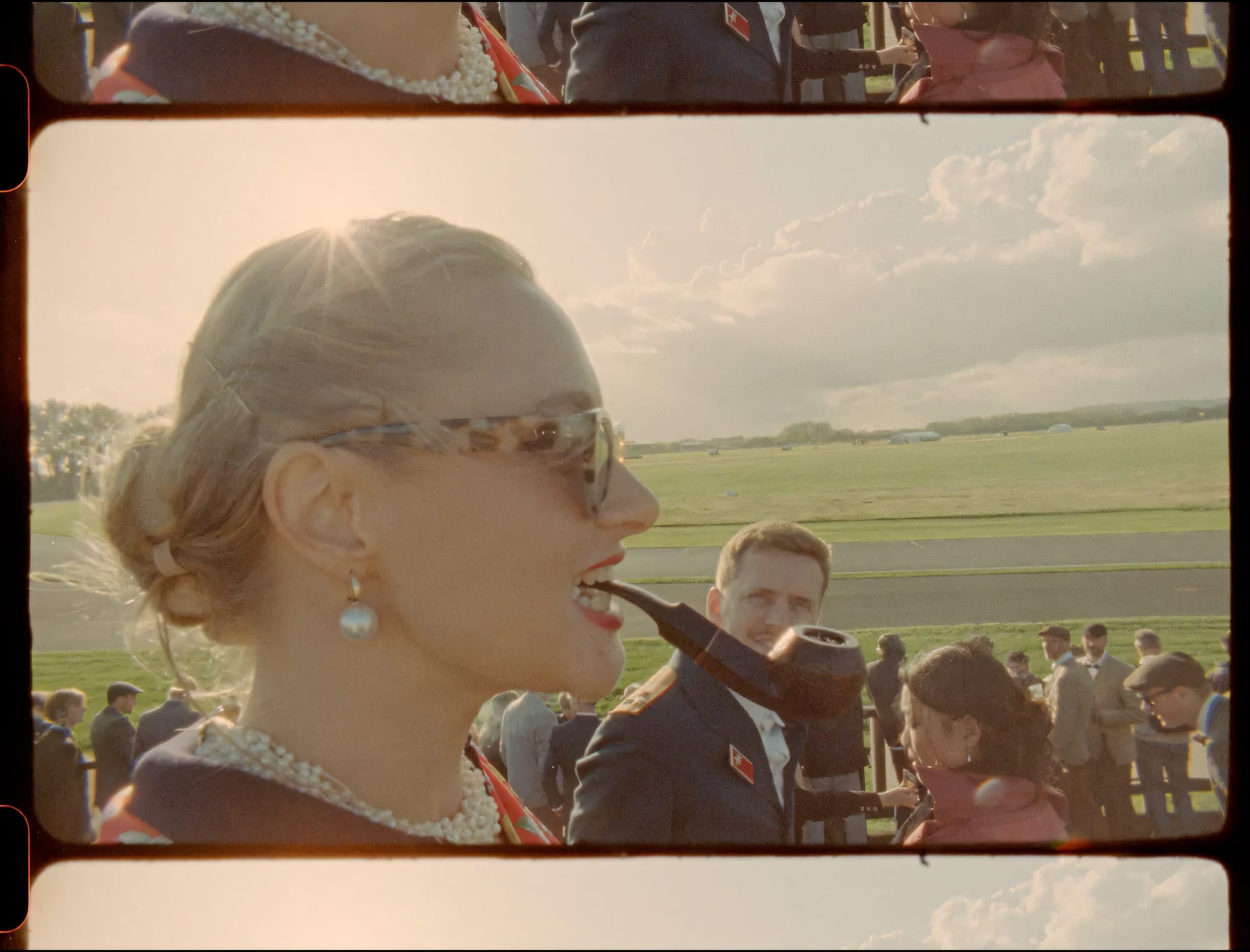 Woman in vintage dress watching racetrack with crowd behind her.
