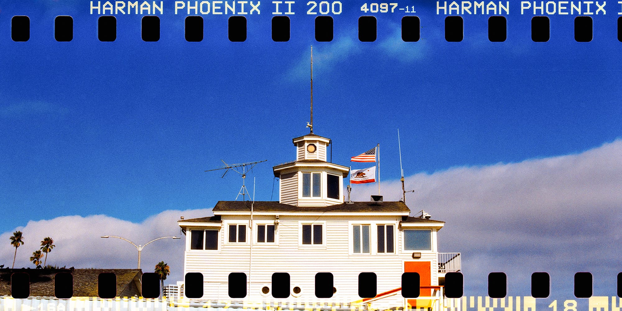 White coastal building with tower and flags against blue sky with visible sprocket holes.