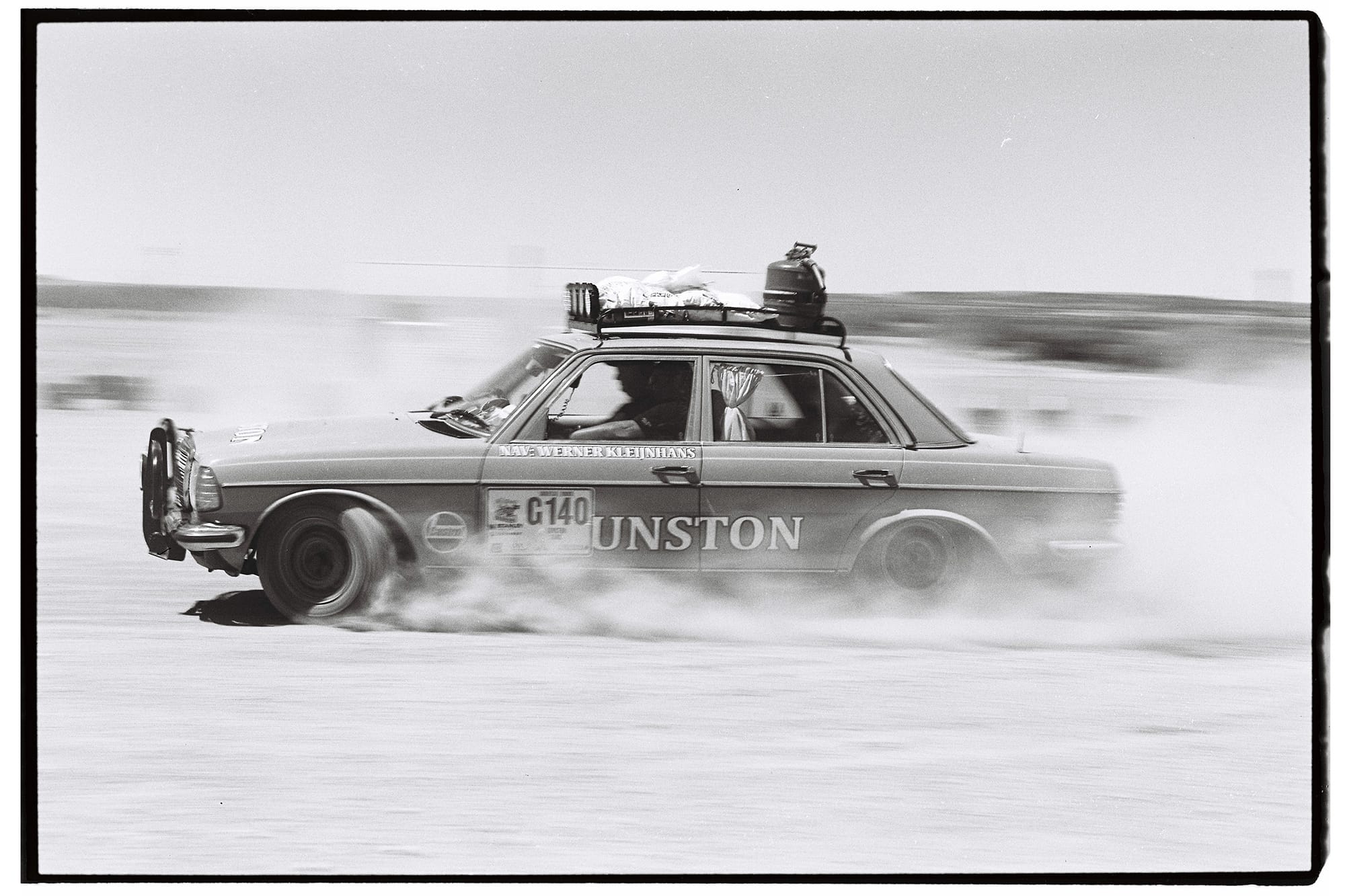 Mercedes sedan kicking up dust cloud while racing.