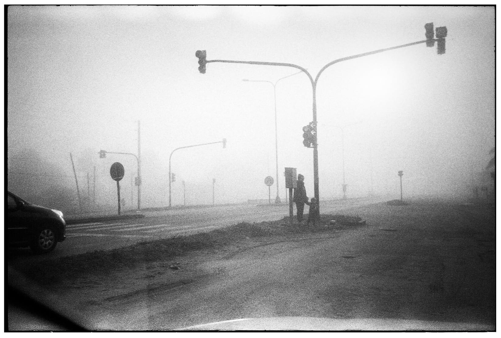 Parent and child walking through foggy intersection with street lights.