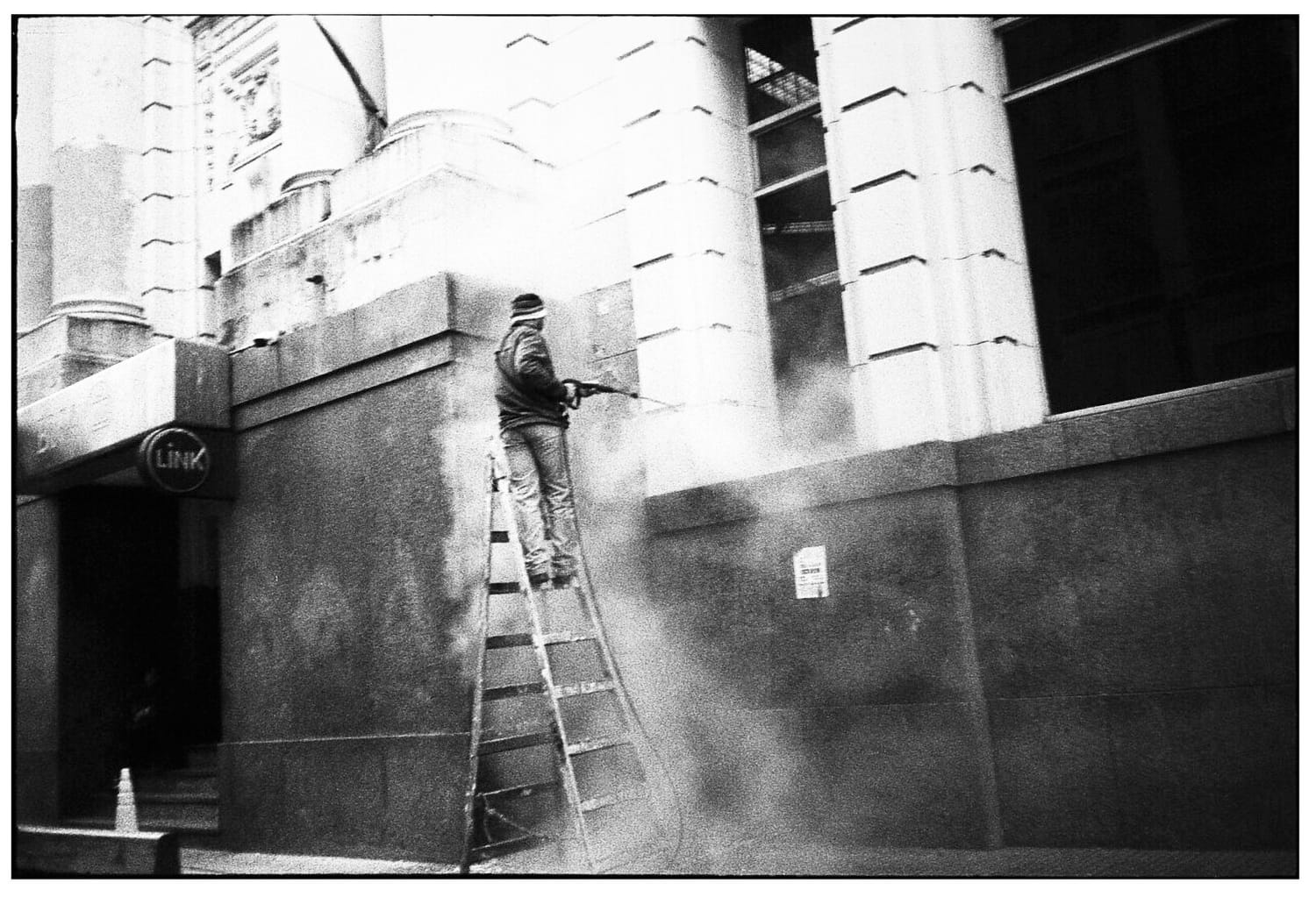 Pressure washer on ladder cleaning exterior wall.