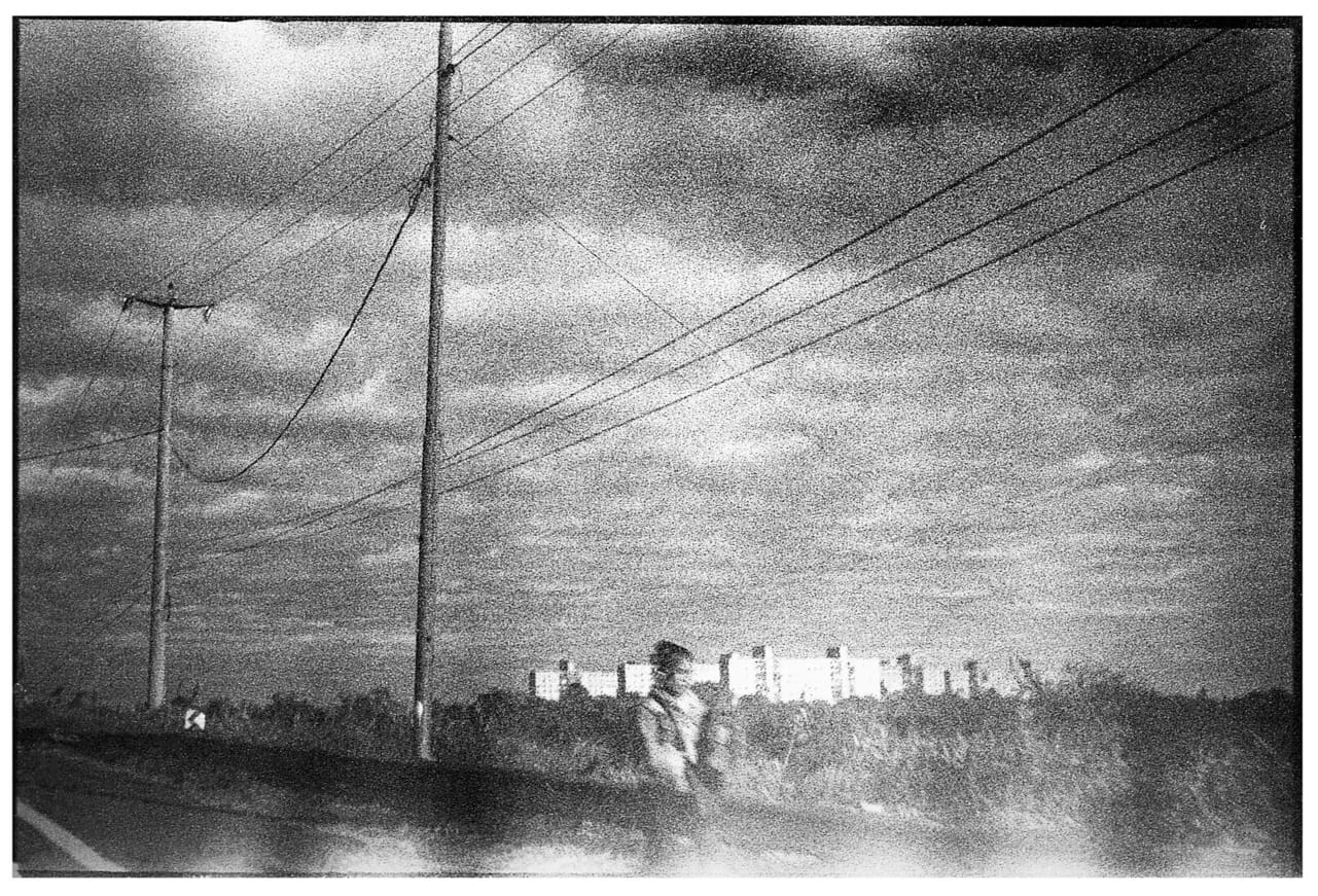 Grainy late-day shot of figure crossing street with power lines.