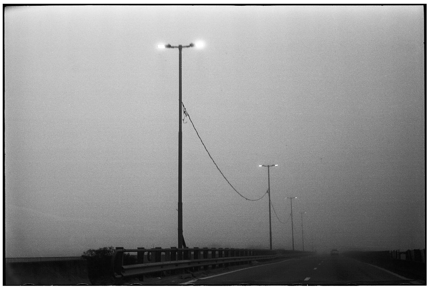 Highway with street lights and sagging power line at dusk.