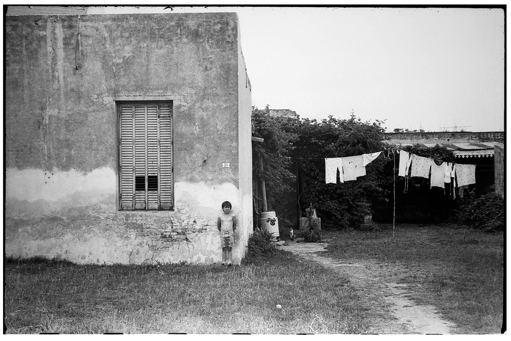 Child standing in front of weathered house with laundry line.