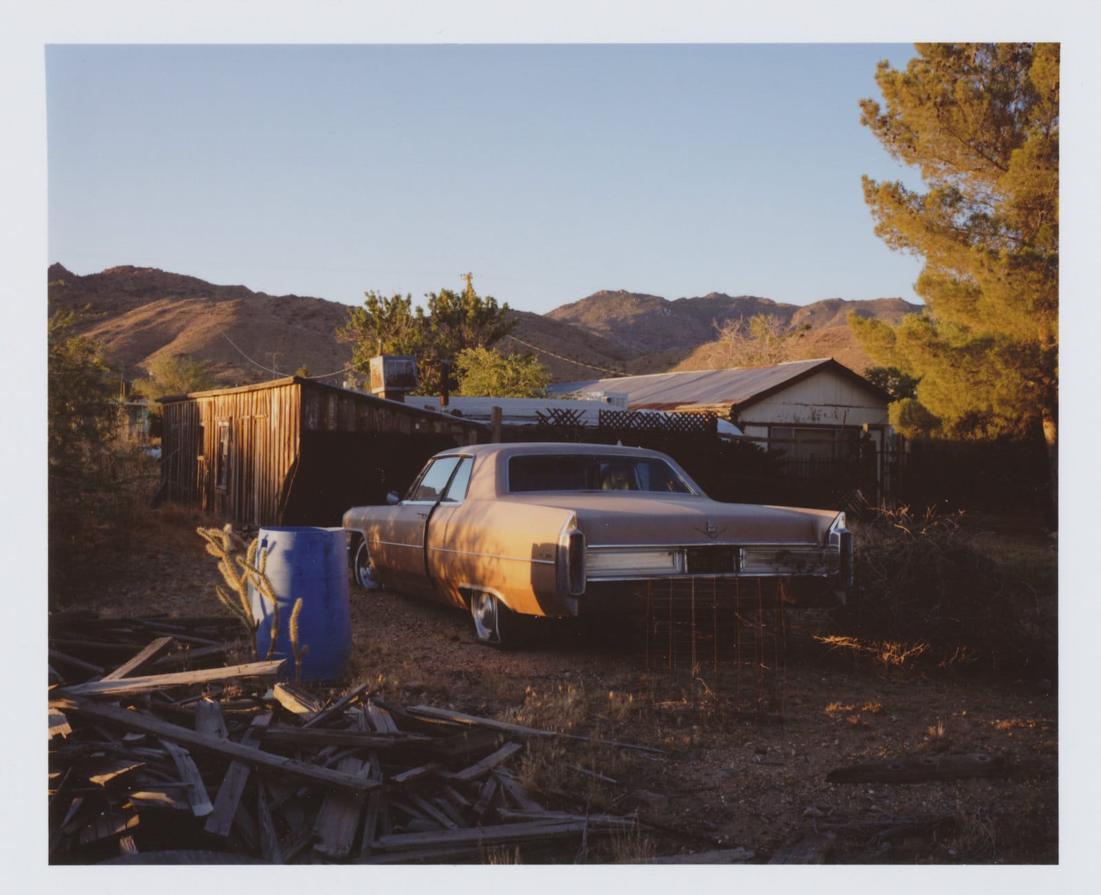 Rusted sedan in desert yard with mountains at sunset.