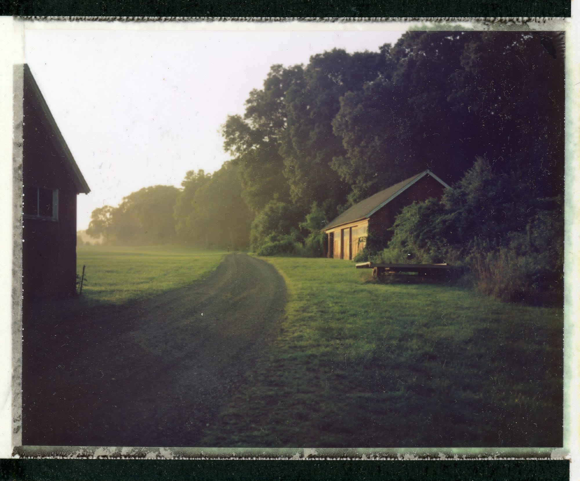 Dirt road between barn structures at sunrise with light leak on instant film.