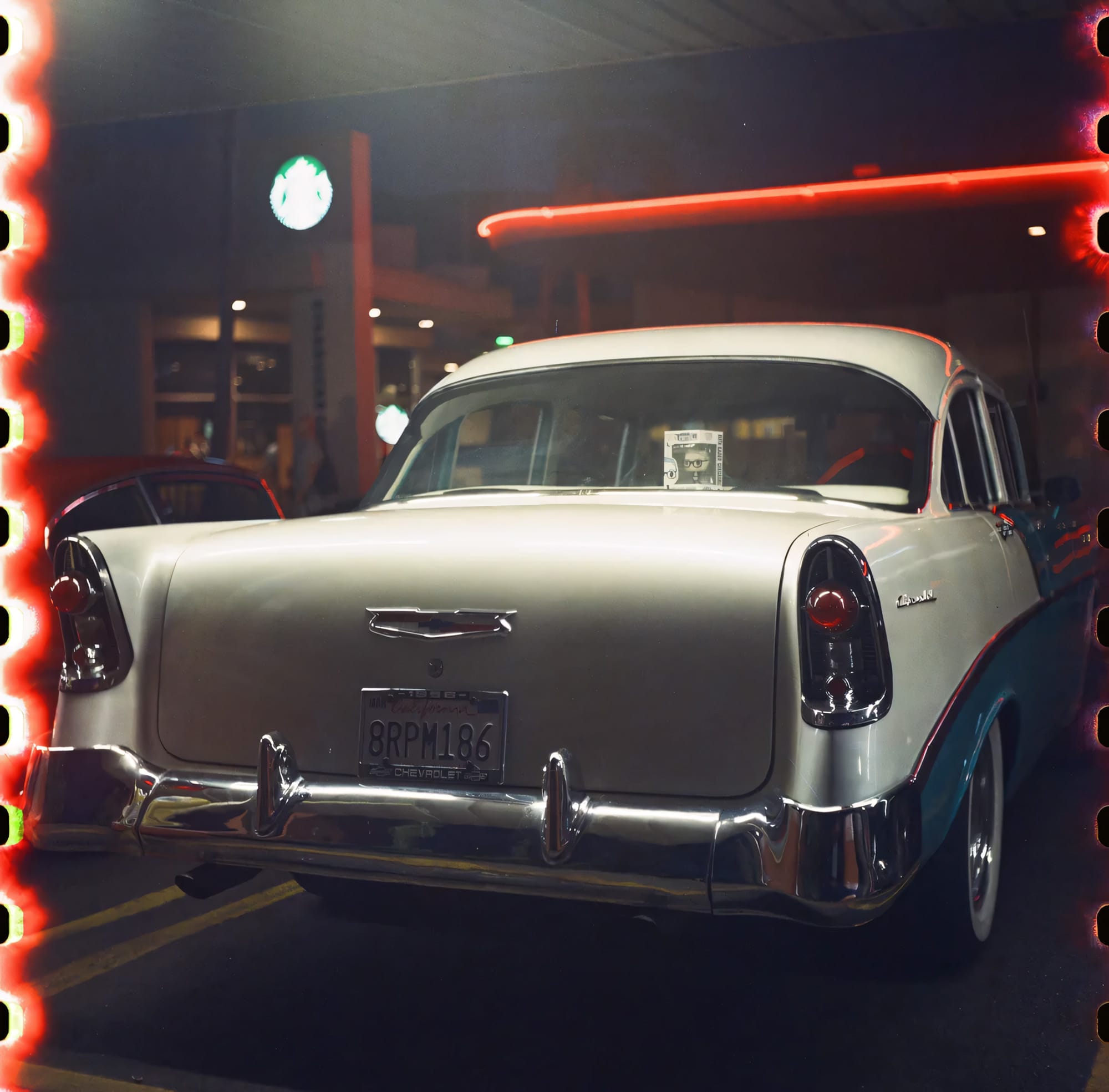 White vintage Chevrolet under neon lights at night with sprocket holes visible.