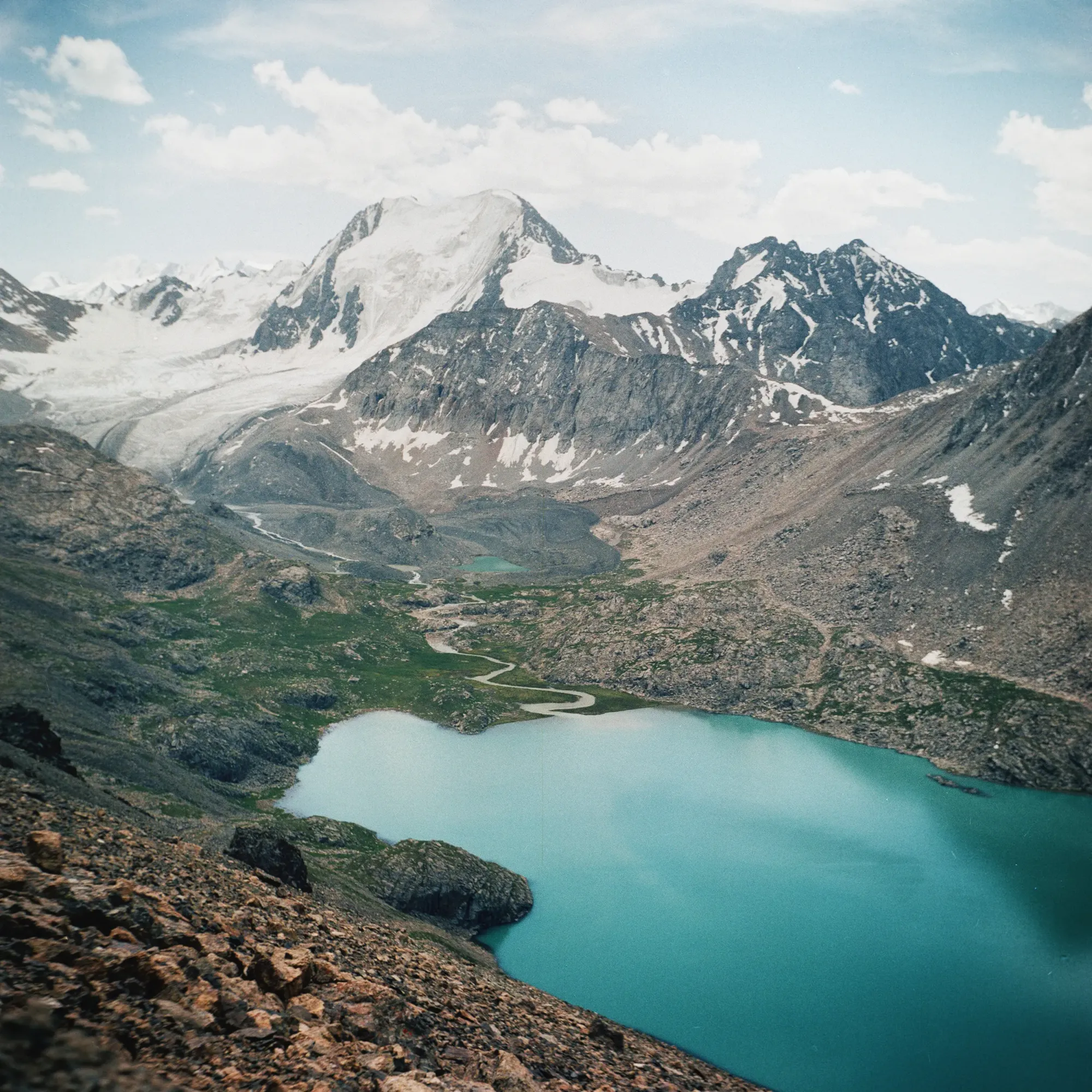 Snow-capped mountain peaks rising above turquoise alpine lakes with winding green valley below.