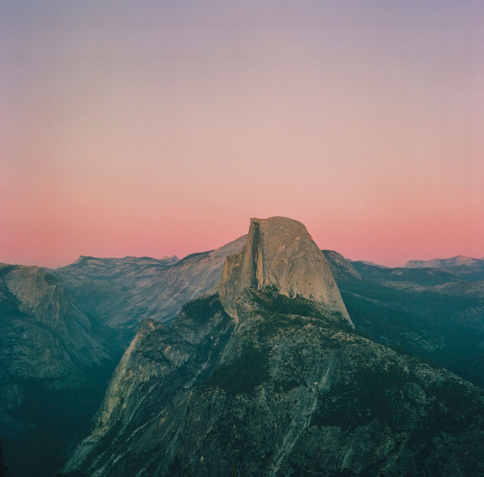 Half Dome stands against pink sunset sky in Yosemite.
