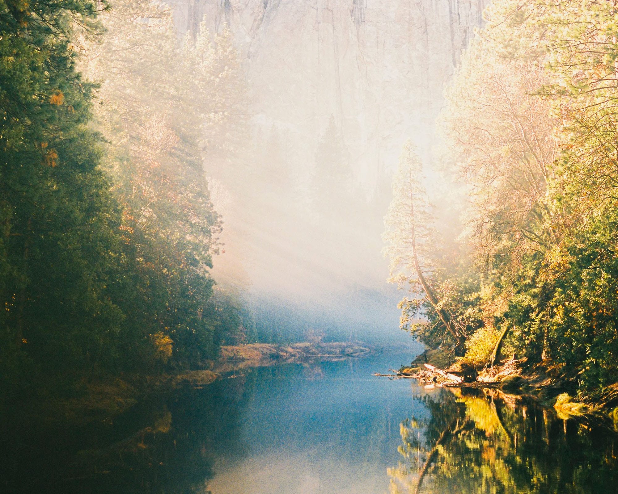 Autumn trees frame misty river with golden foliage reflected in water.
