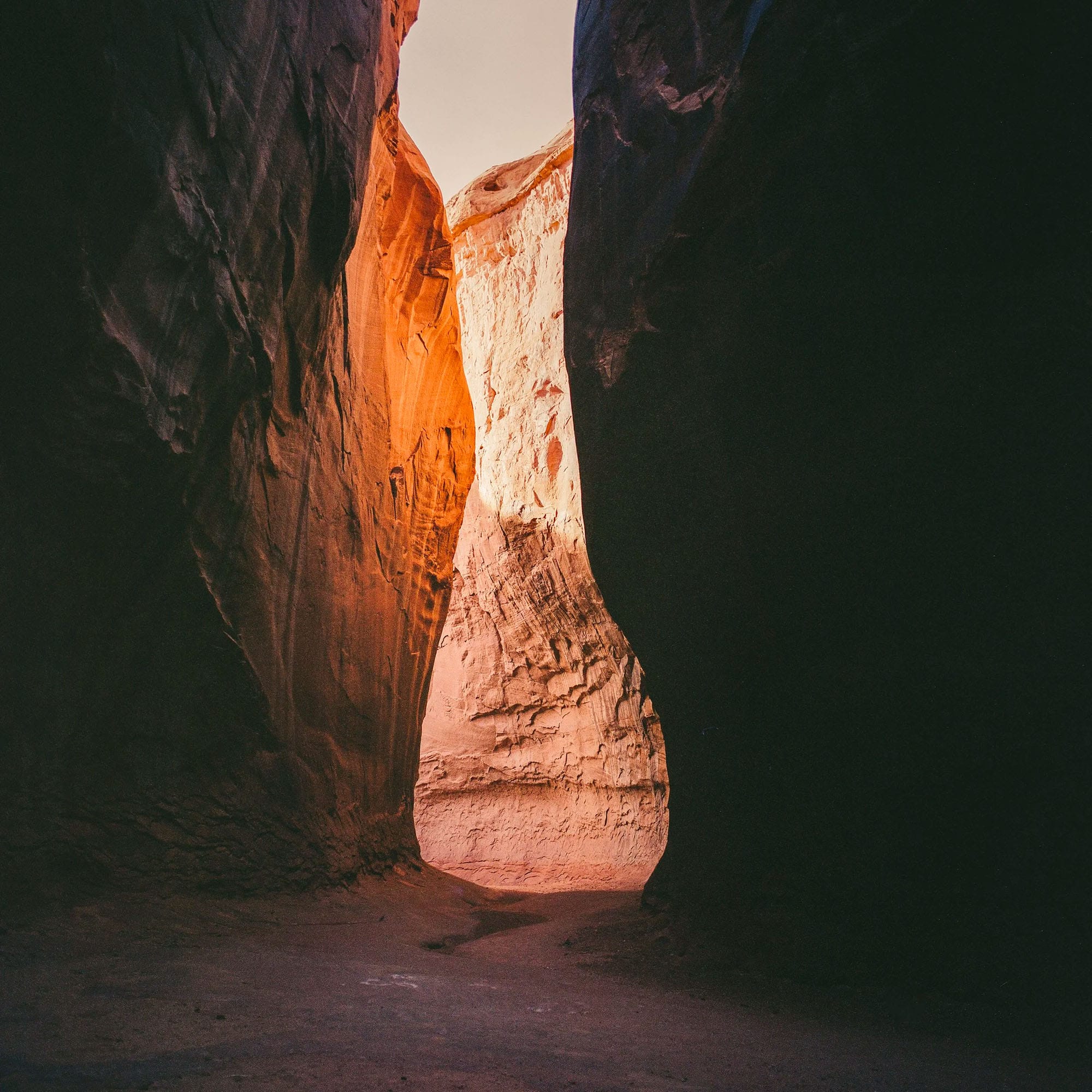 Narrow slot canyon shows orange sandstone walls with light filtering through.