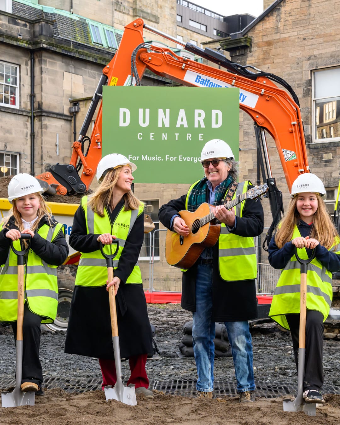 People wearing luminous vests holding musical instruments and spades at a building site. 