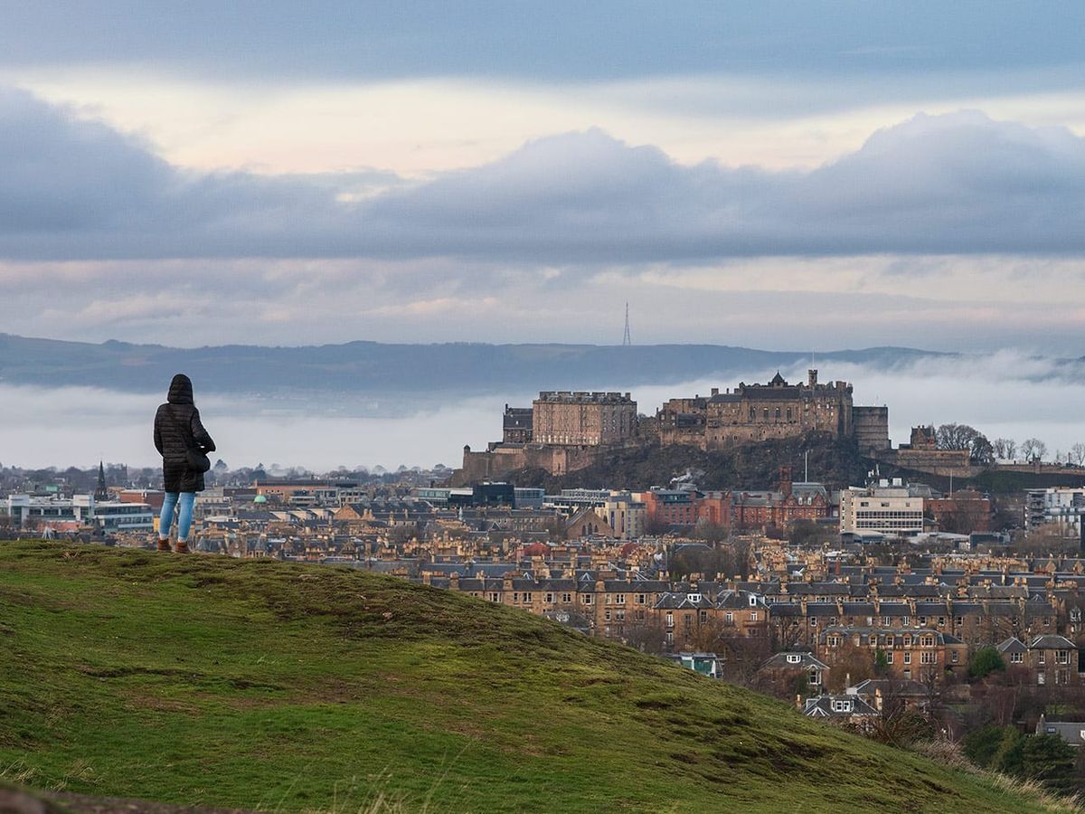 A person standing on a hill in the foreground with a city skyline in the background. 