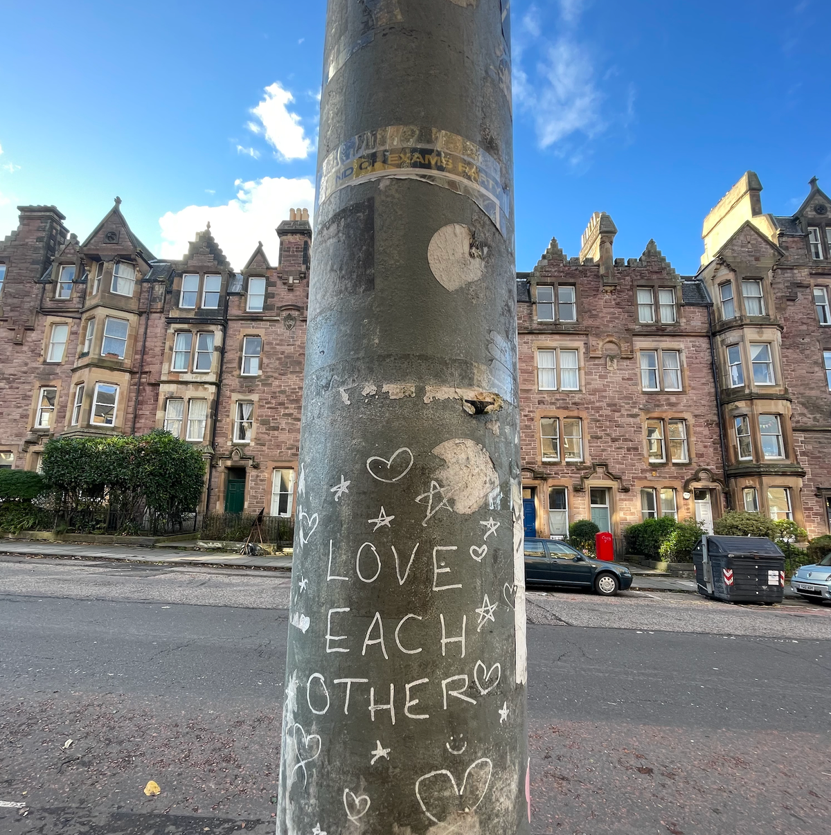 A residential street with 'love each other' written on a lamppost in the foreground