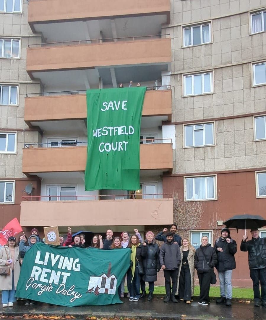 A group of people holding banners standing outside a block of flats. 