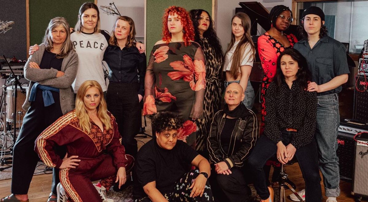 Twelve people standing in a studio in front of musical equipment. 