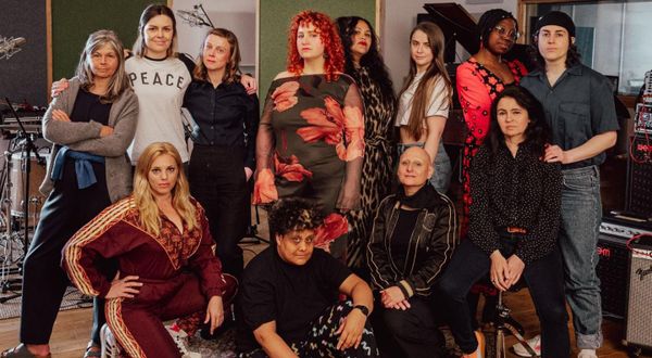 Twelve people standing in a studio in front of musical equipment. 