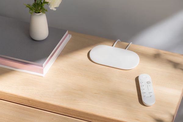 The Google TV Streamer (Porcelain) sitting on a table next to its remote.
