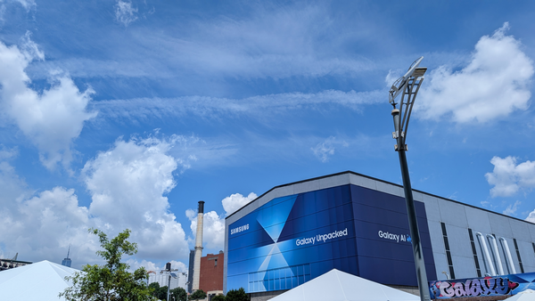 A photo of a building with a Galaxy Unpacked banner over it and a smoke stack in the background