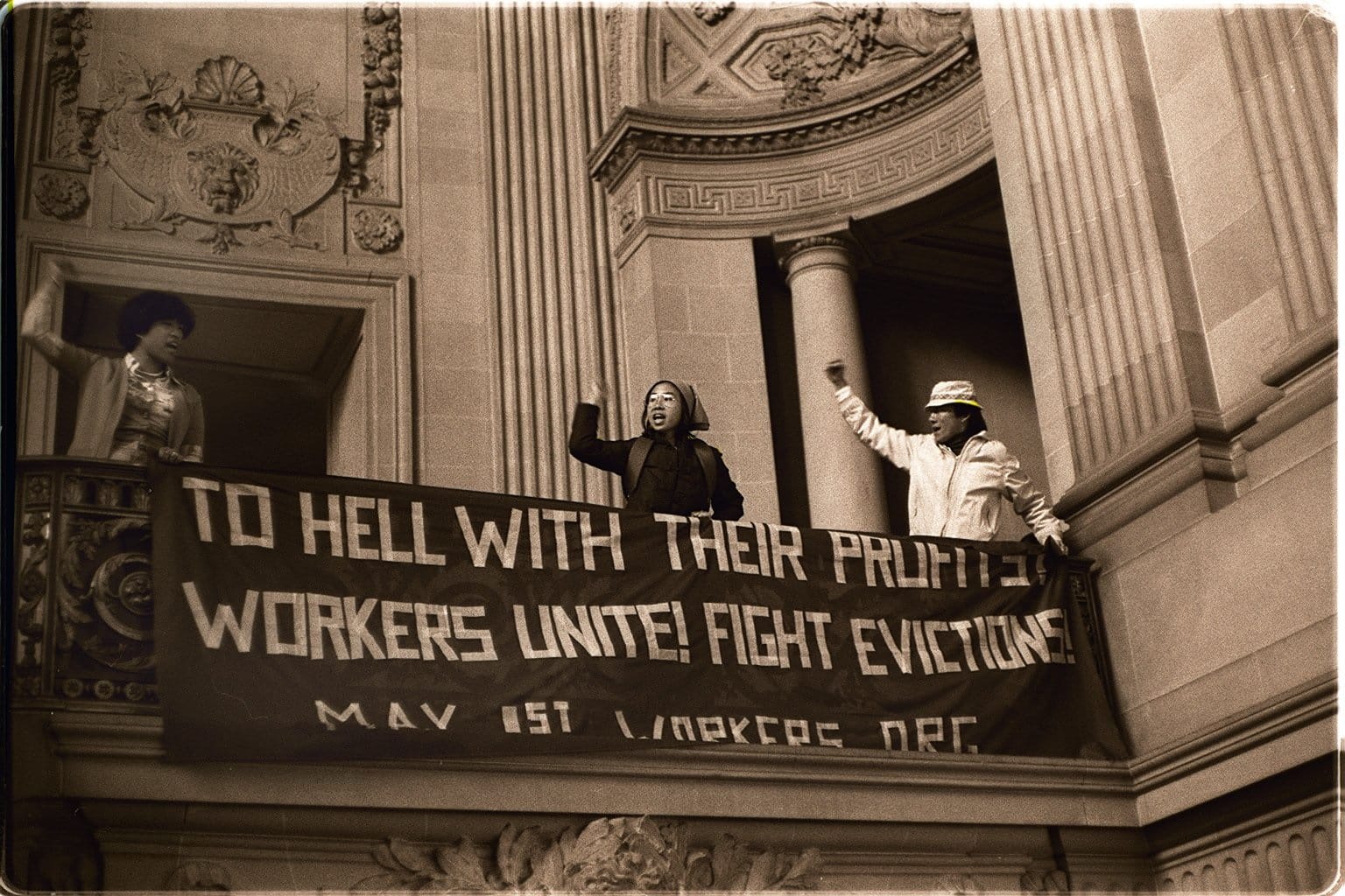 Three protesters at San Francisco's City Hall holding banner that reads "To hell with their profits! Workers unite! Fight evictions! Credit Nancy Wong