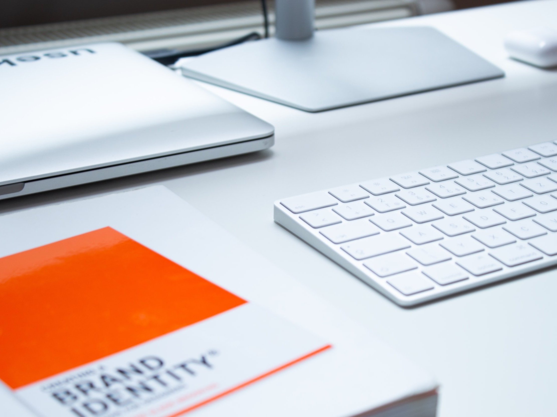 An Apple laptop and keyboard, with a book titled "Brand Identity" on the side.