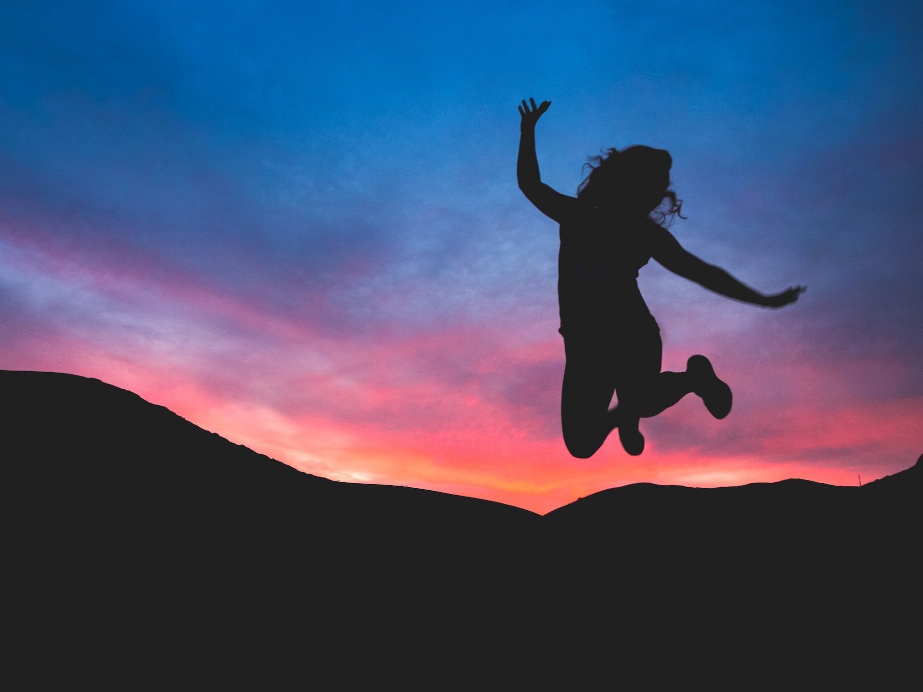 With a vibrant pink and blue sky in the background, a lady is jumping for joy.