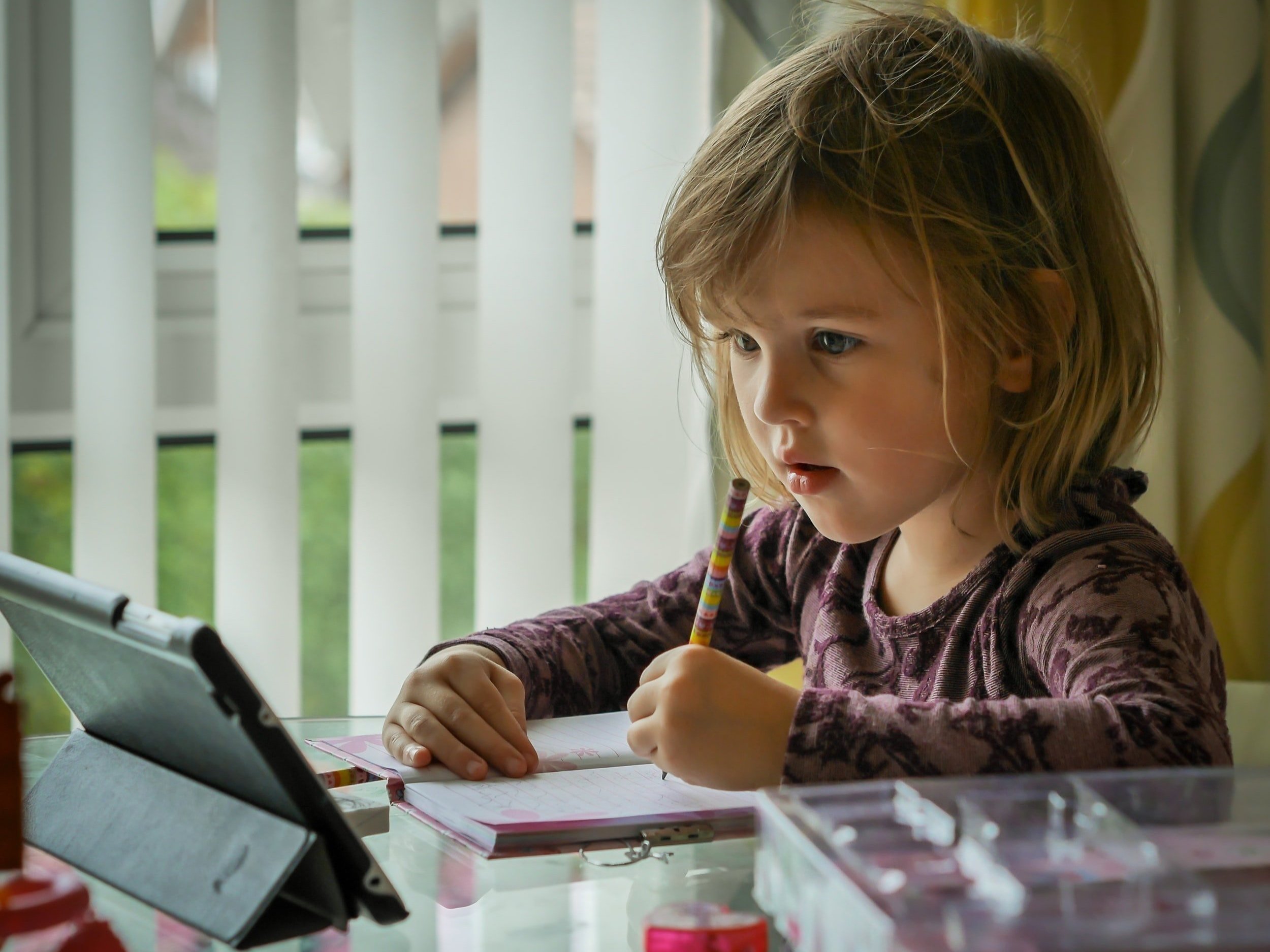 A young girl is writing and learning in front of an Apple iPad.
