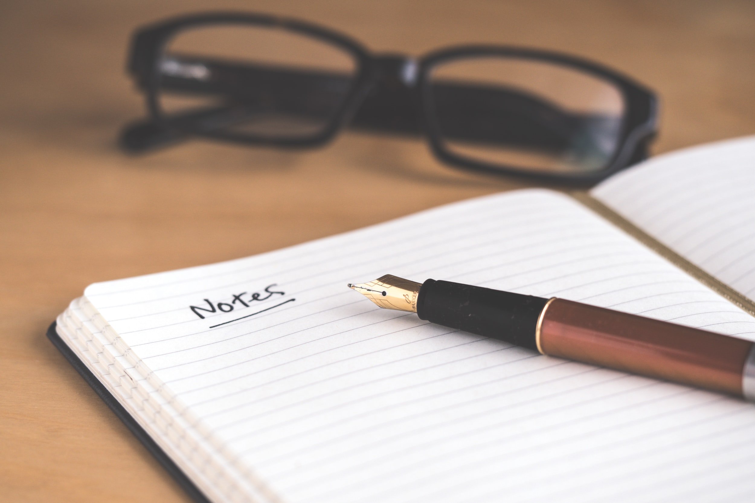 A notepad with the word notes written in ink sits on a desk alongside a pair of glasses.