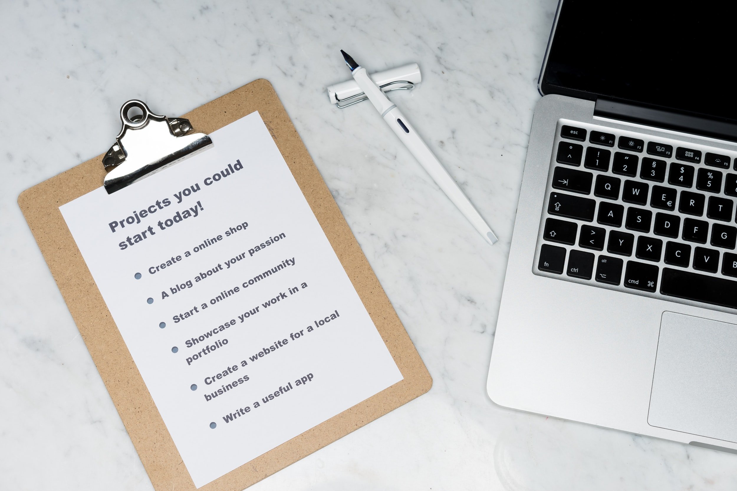 A clipboard with a list of projects that could be started today next to a pen and an Apple MacBook Air.