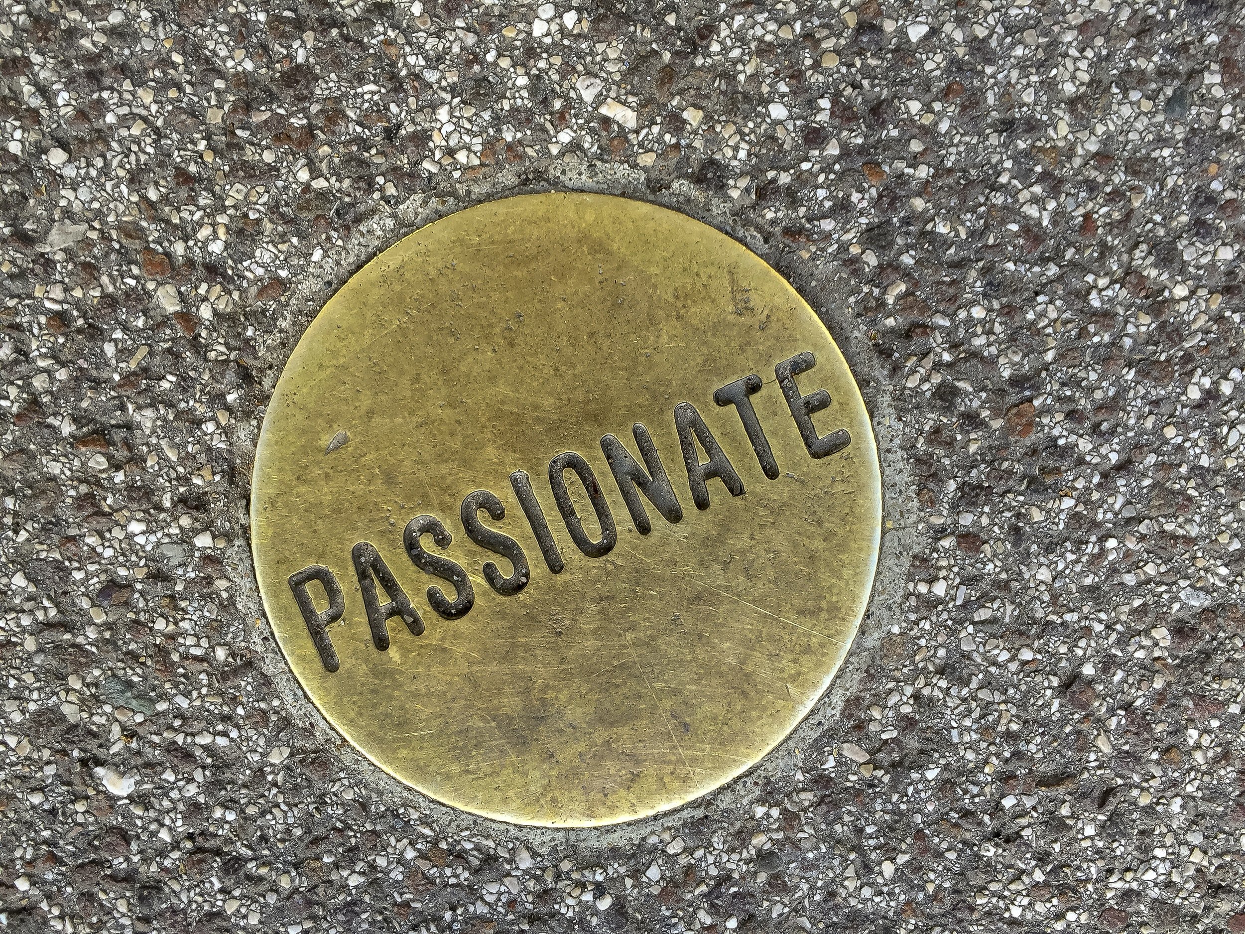 A brass plate with the word "Passionate" on it on the pavement.