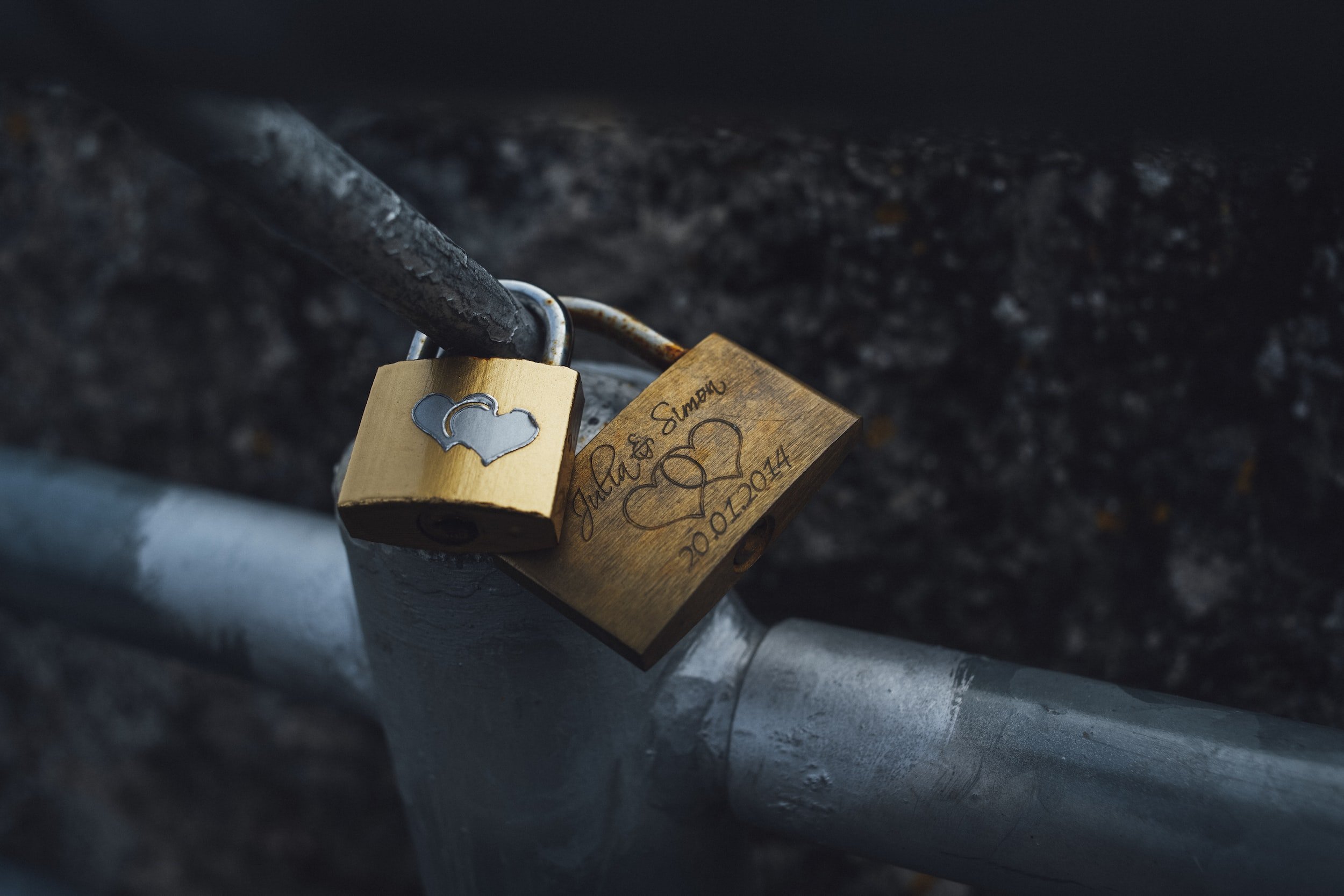 Two padlocks with engraved love hearts are secured to a metal bar.