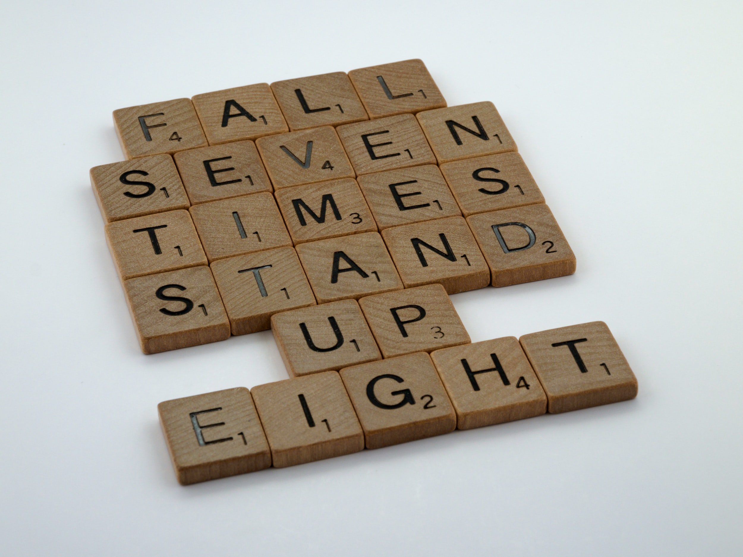 The phrase "fall seven times, stand up eight" is written in wooden letter tiles.