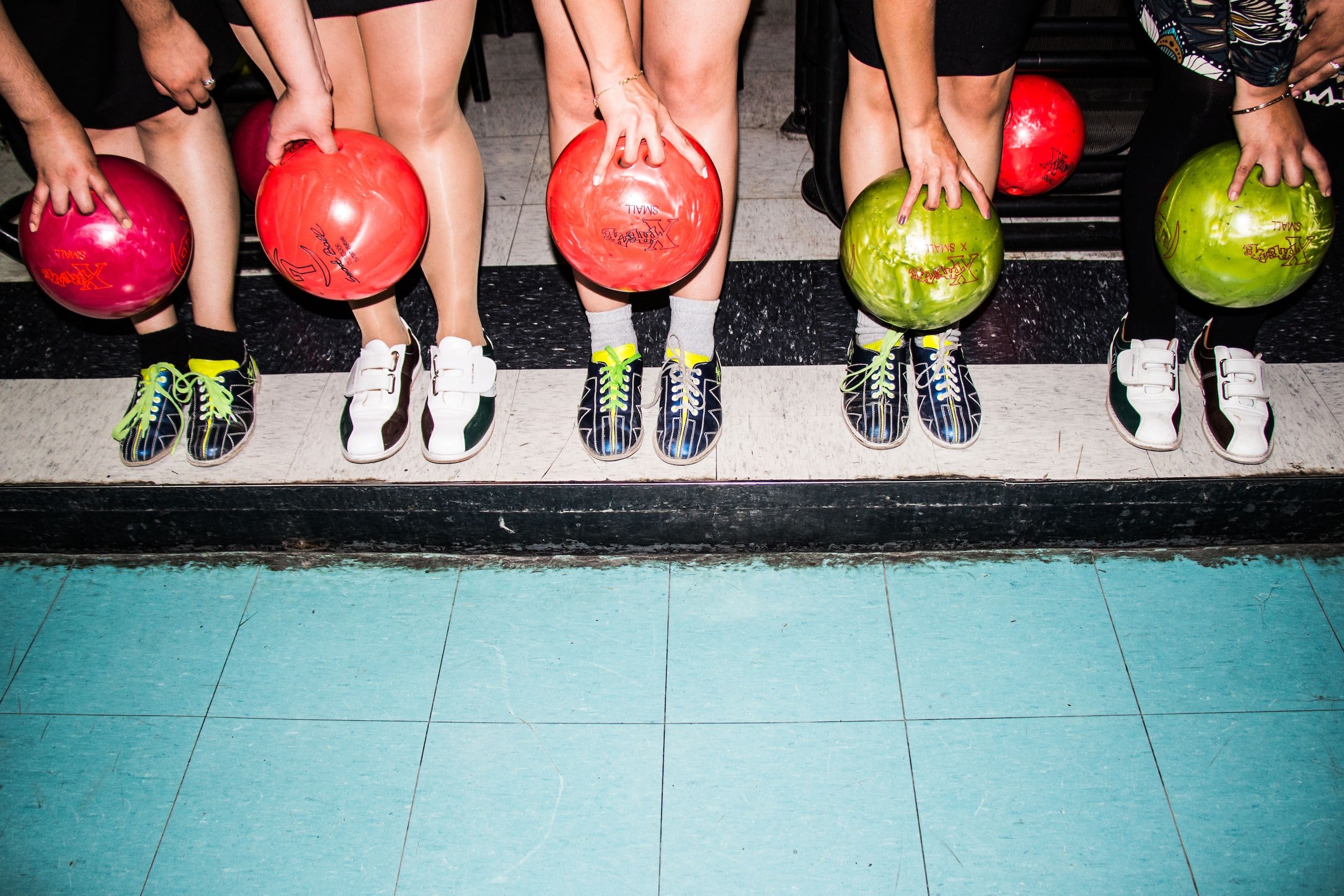 Five people stood in a row, each holding a bowling ball and wearing bowling shoes.