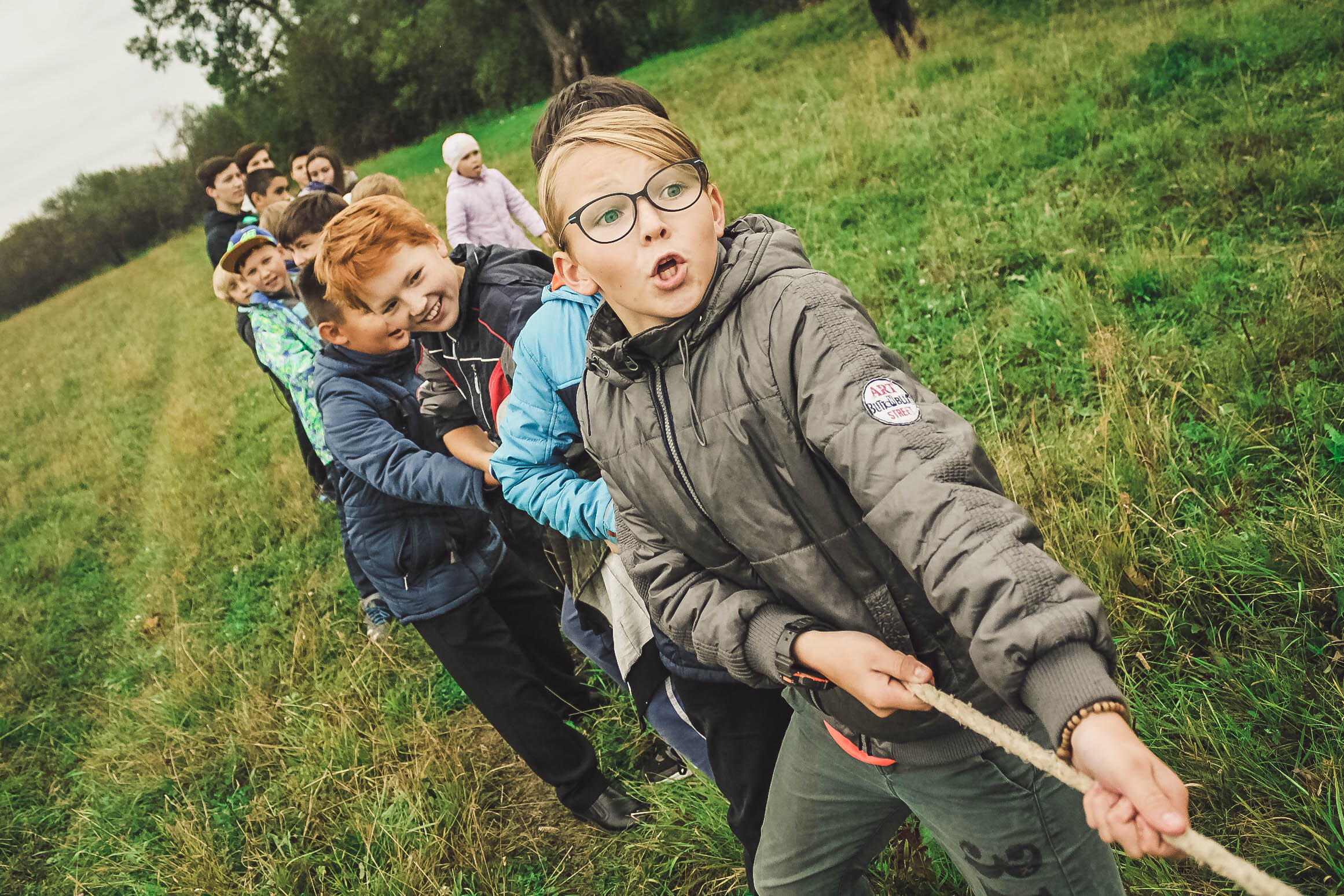 A large group of children and young adults are pulling on a rope in a game of tug of war.