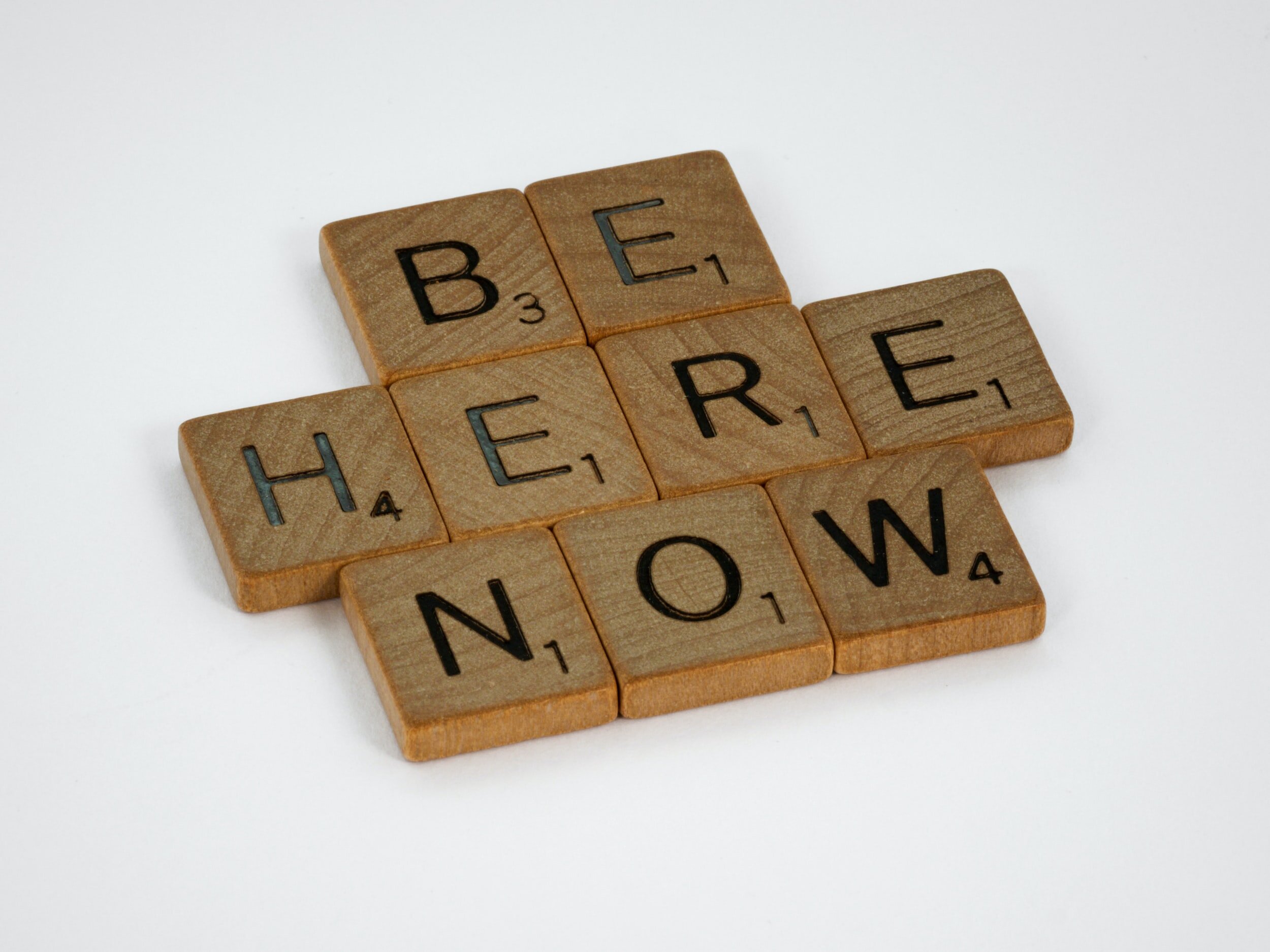 "Be Here Now" is written in wooden letter tiles.