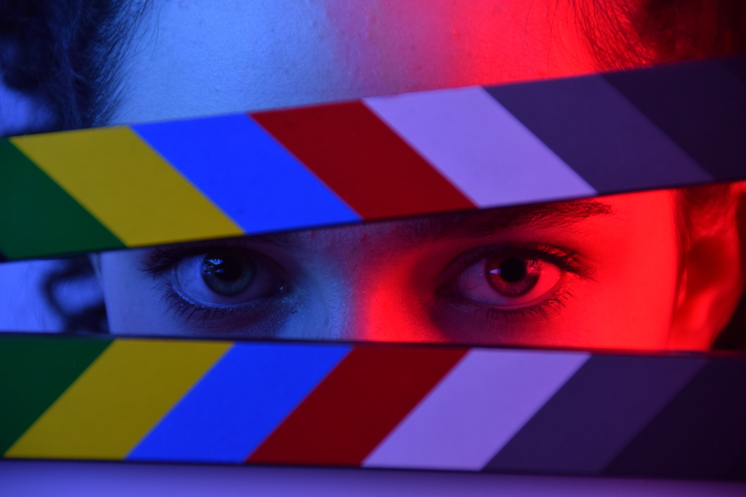 A person looks through a Director's clapperboard with a red light reflection on the side of her face.