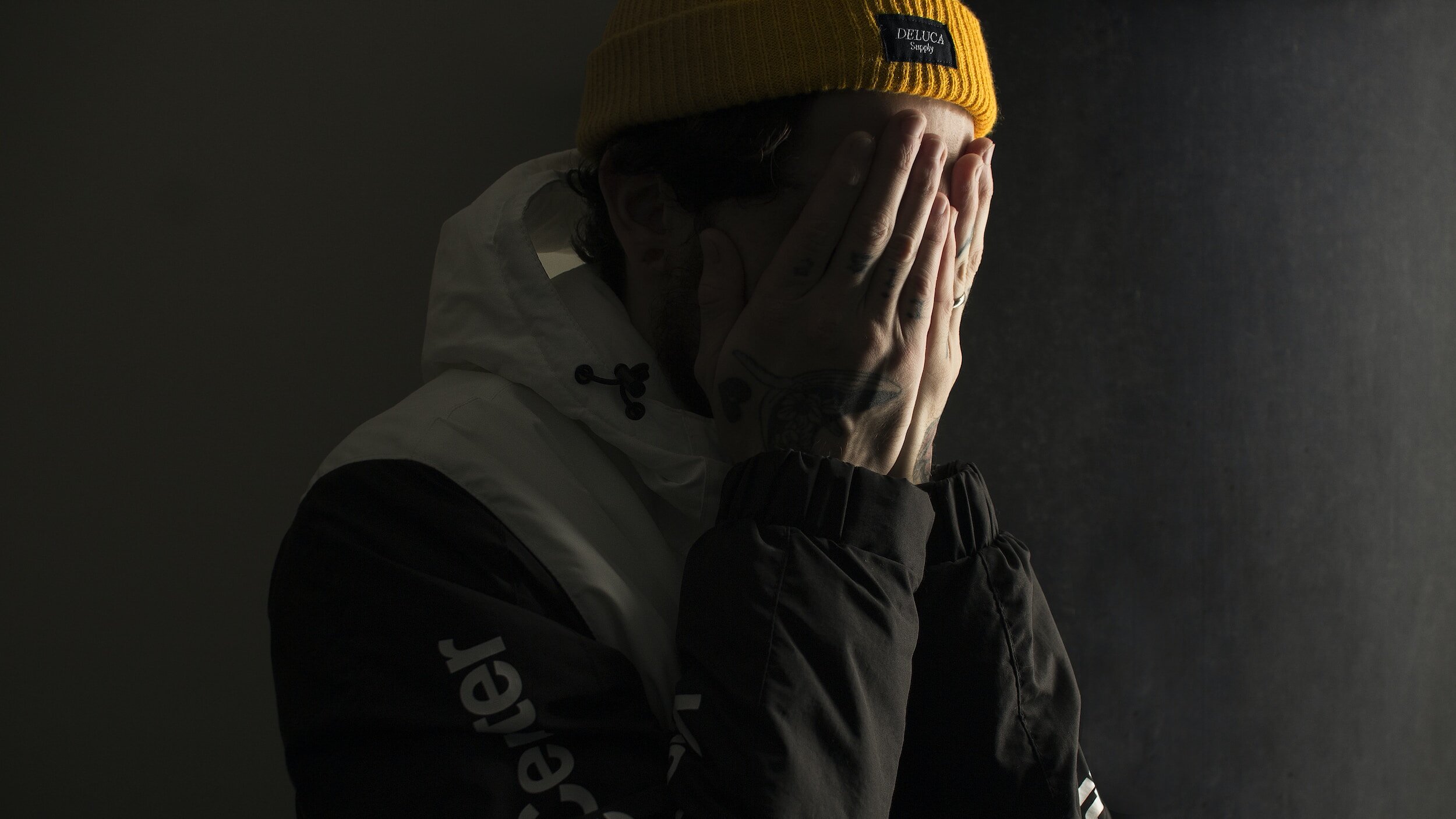 A man with his head in his hands, wearing an orange beanie.