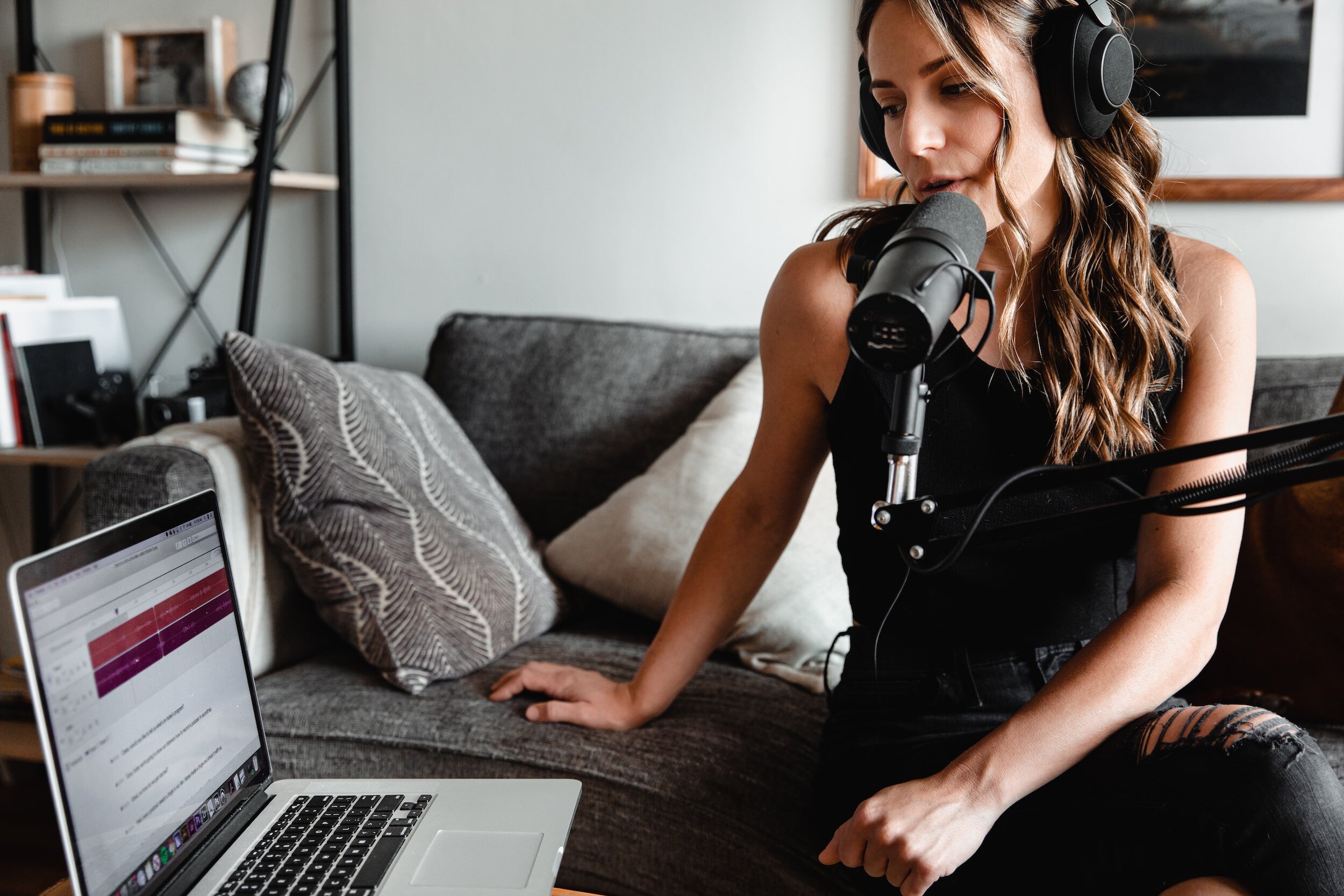 A person producing a podcast while seated on a couch with headphones and a microphone.