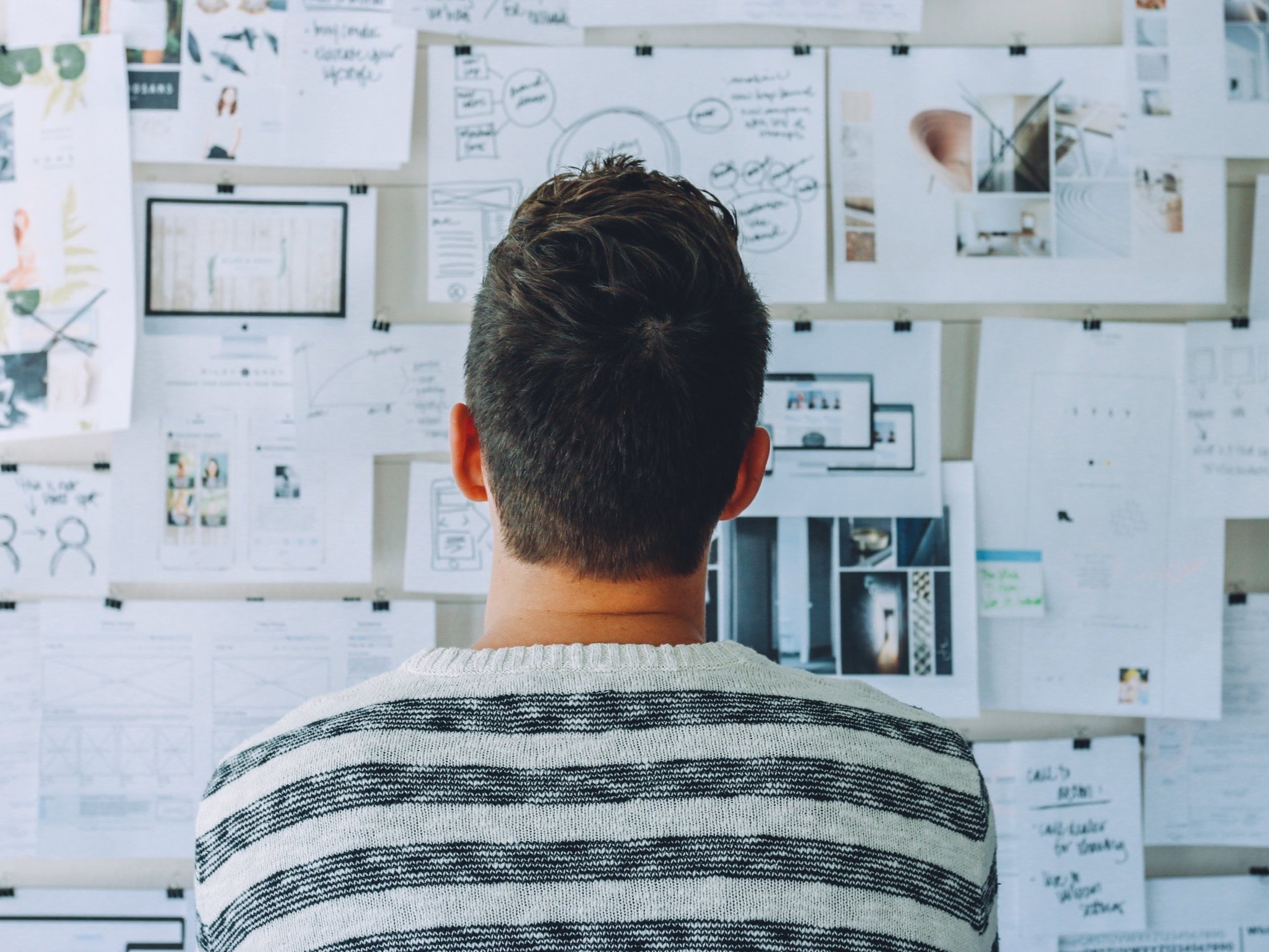 A man with a black-and-white striped shirt examines documents on the wall and considers potential outcomes.