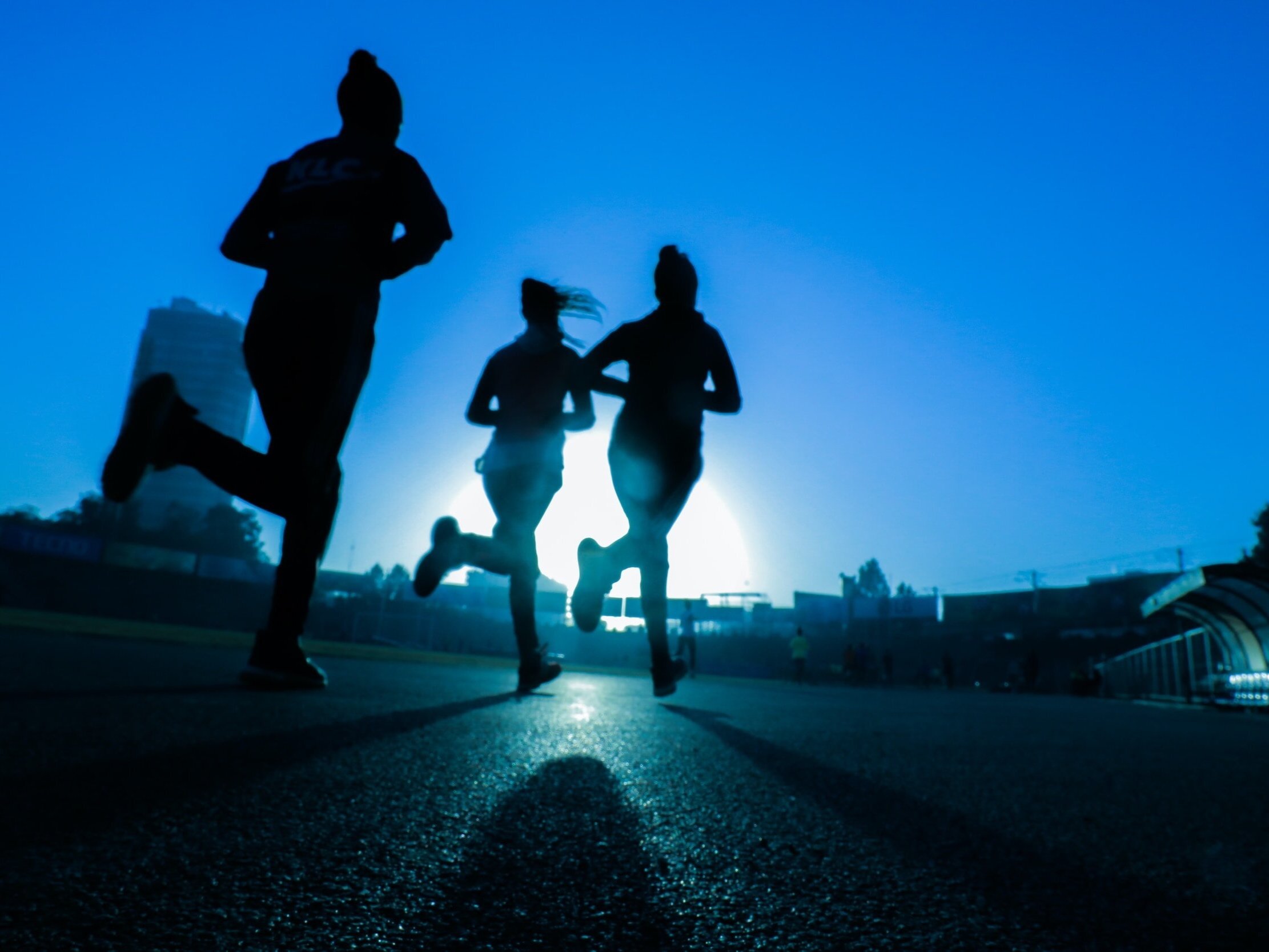 Silhouettes of three people jogging at dawn with a clear blue sky in the background, symbolising a healthy and active lifestyle.