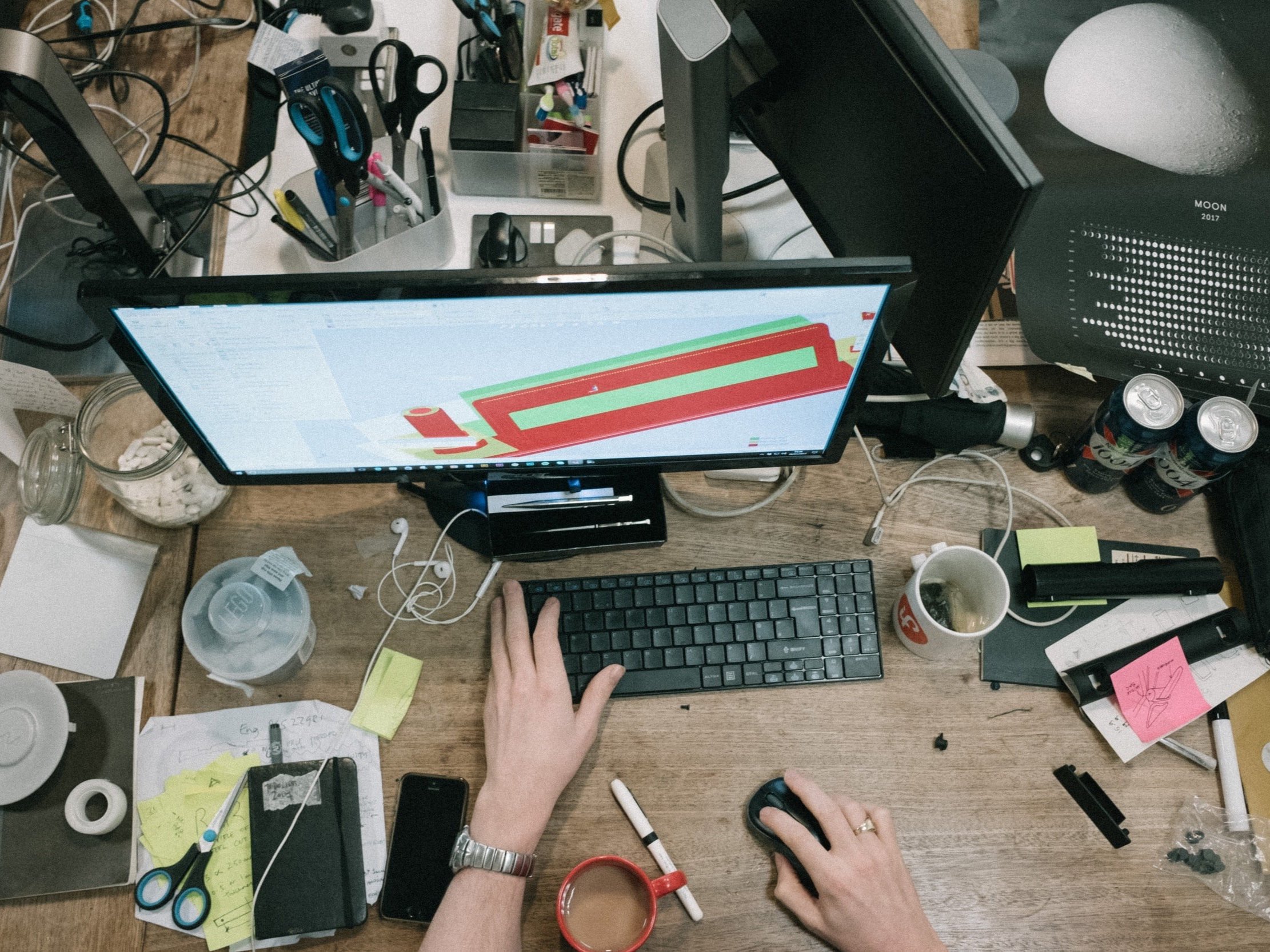A designer working on a computer at a cluttered and busy desk.