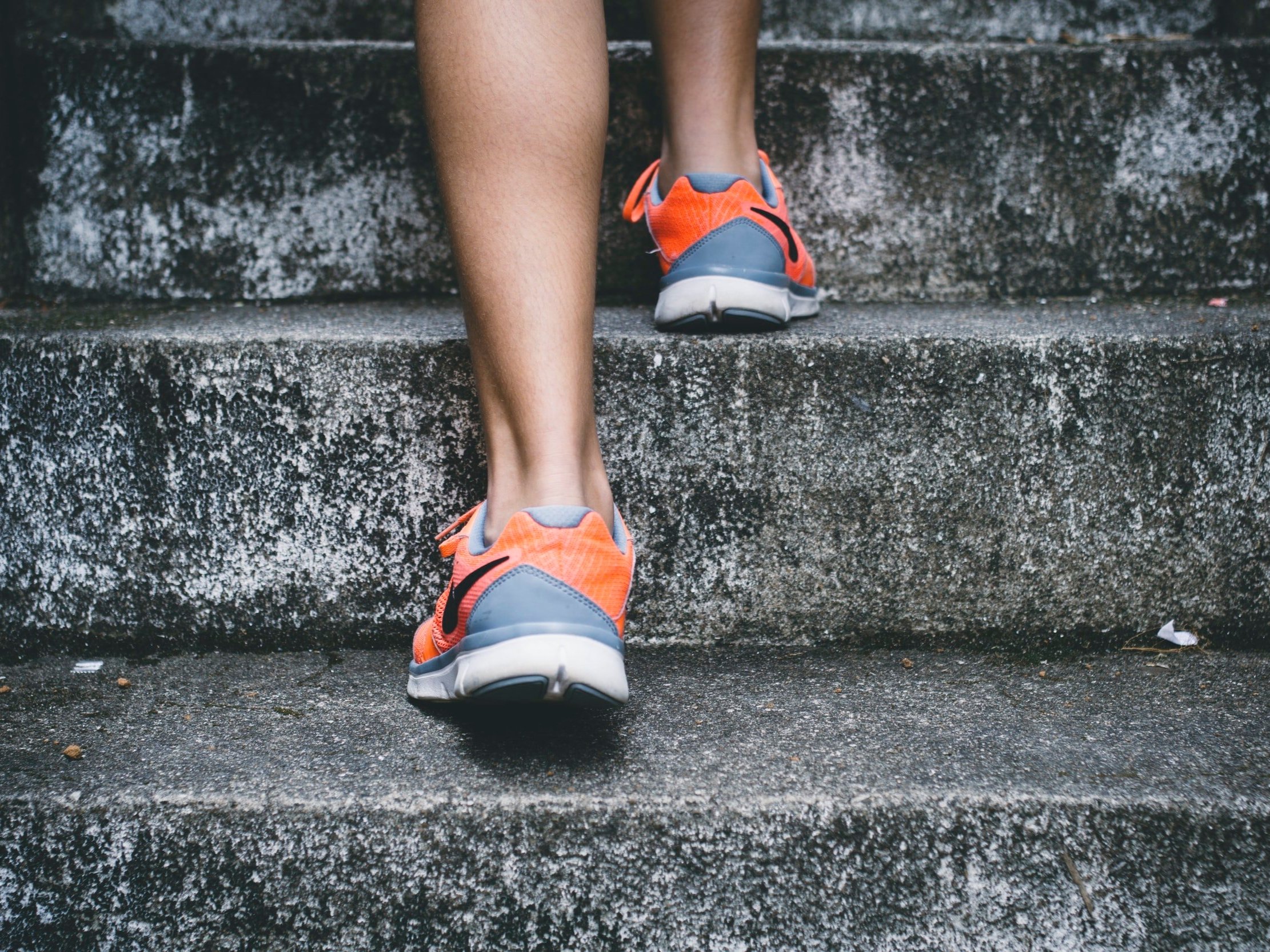 A person wearing running shoes goes up some concrete stairs.