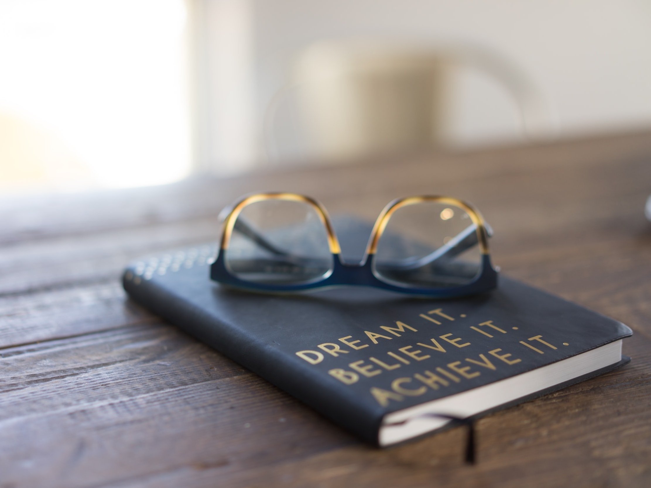 The words "Dream It." "Believe It. and Achieve It." are printed on a leather-bound journal/notepad.