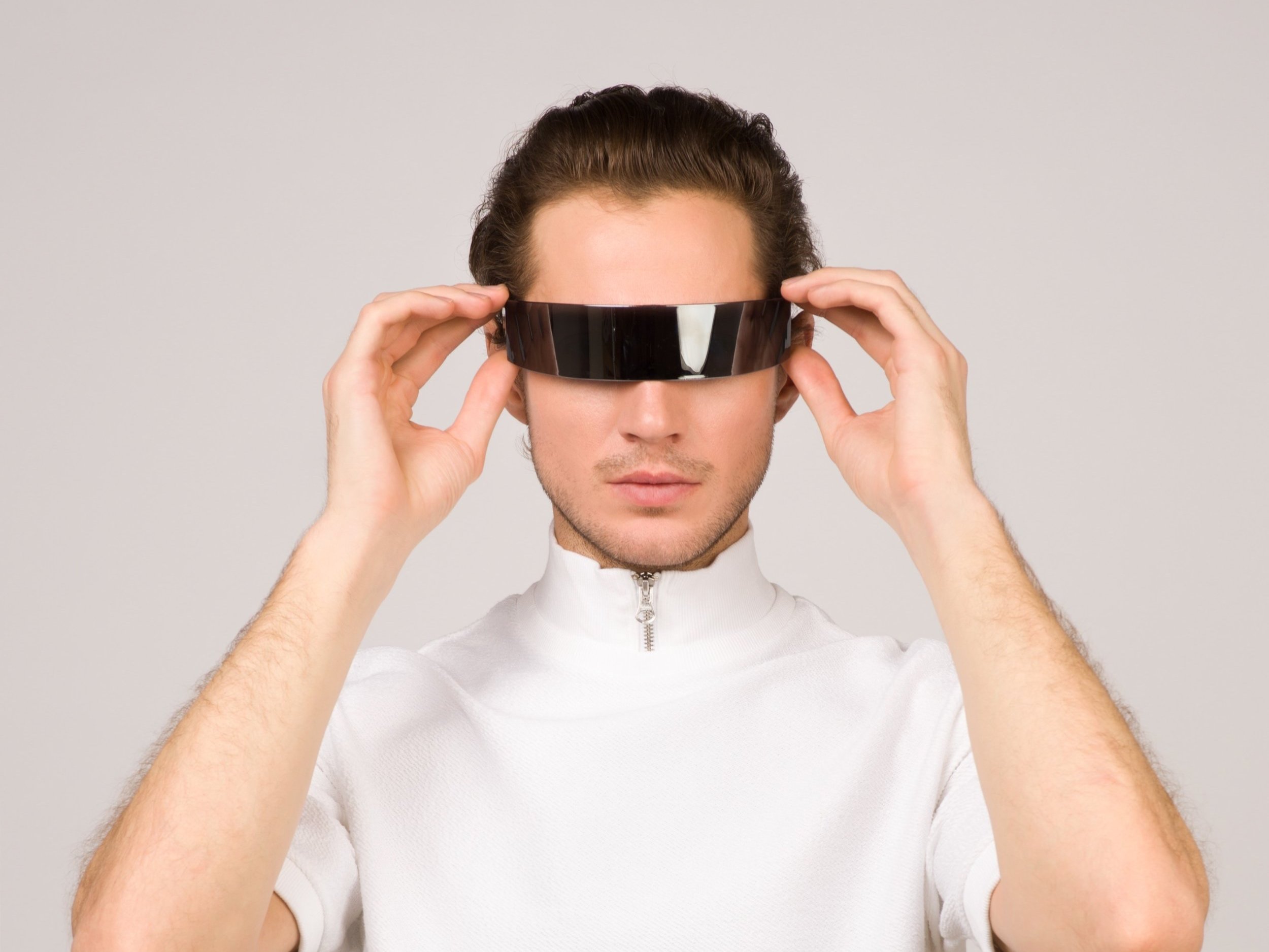 A man wearing a white turtleneck t-shirt and futuristic dark wraparound sunglasses.