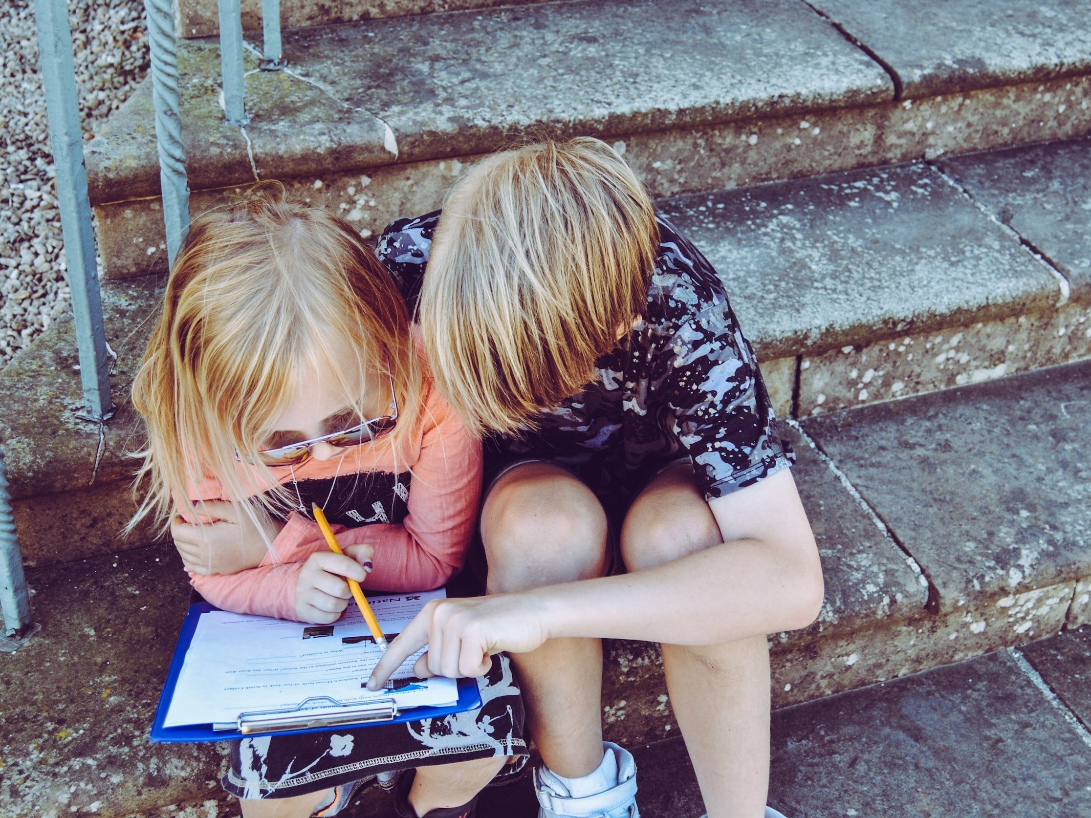 A young boy sits beside a young girl to assist her with her homework.