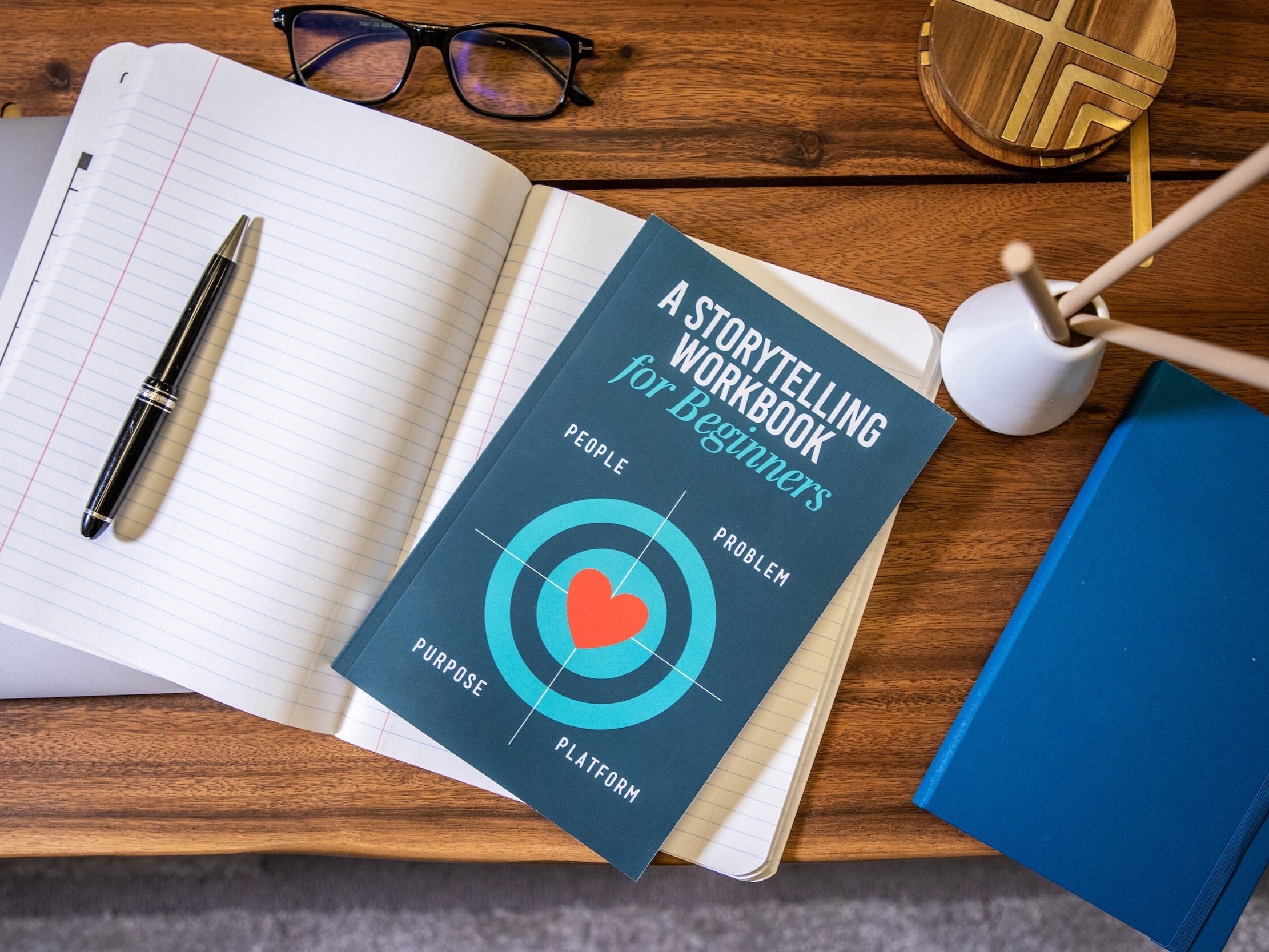 A notebook with lined paper, a pen, and a book titled "A Storytelling Workbook for Beginners"