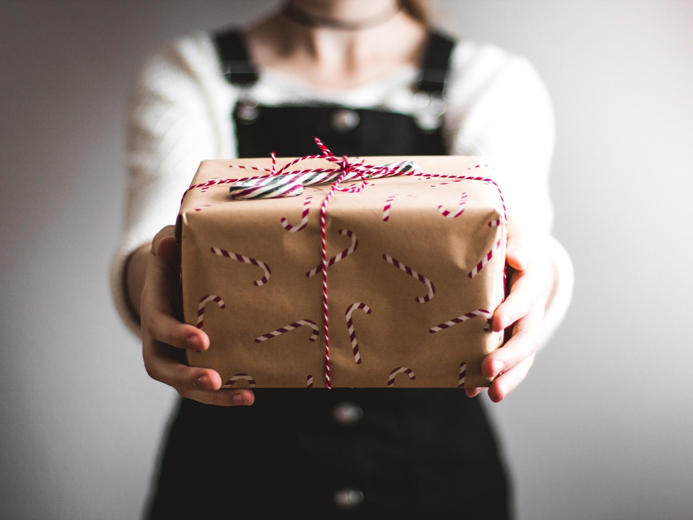 Someone is holding a candy cane paper wrapped gift that has been tied with red and white string and has a candy cane under the bow.
