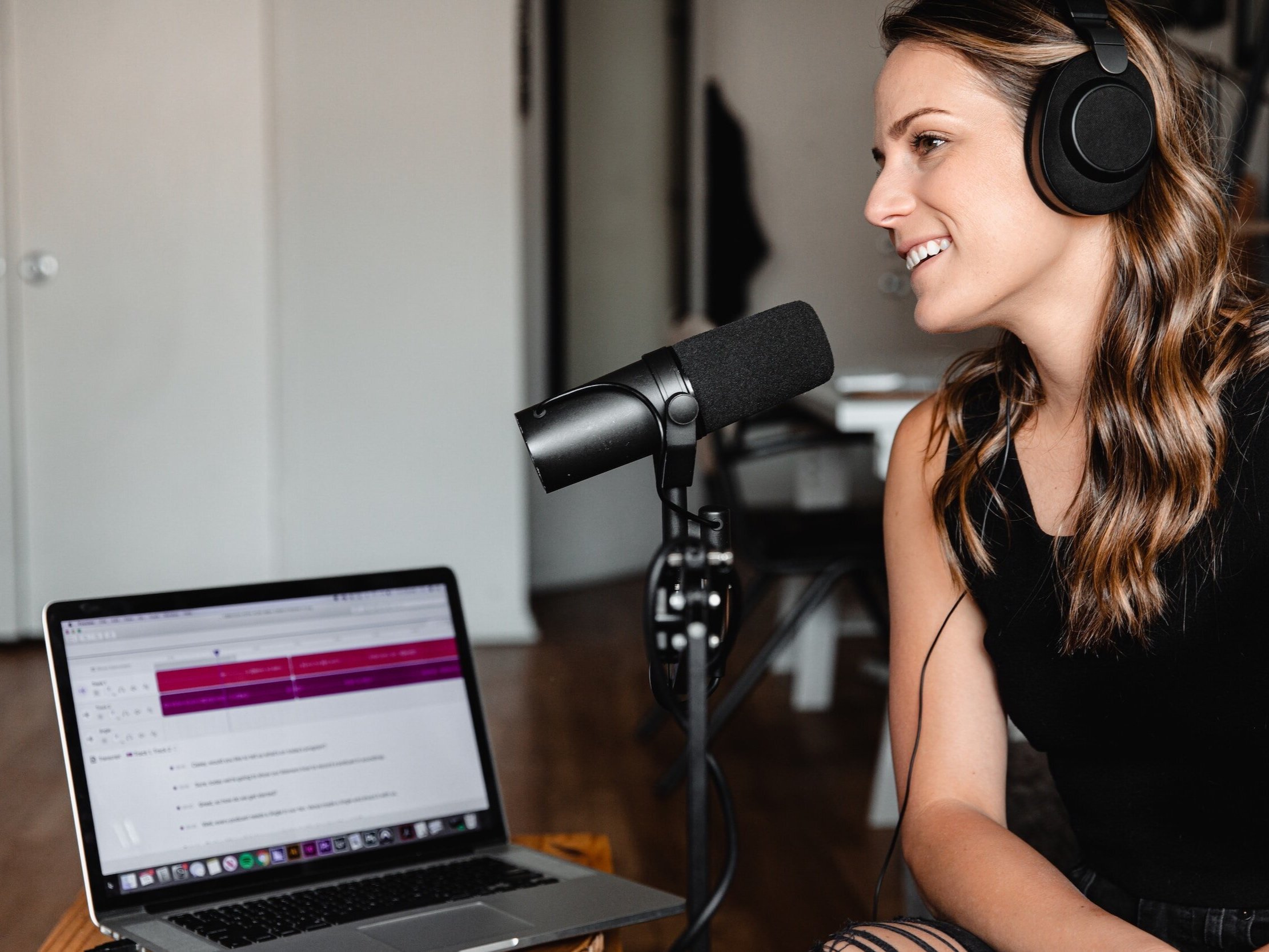 A woman smiles as she sits in front of her microphone for her podcast.