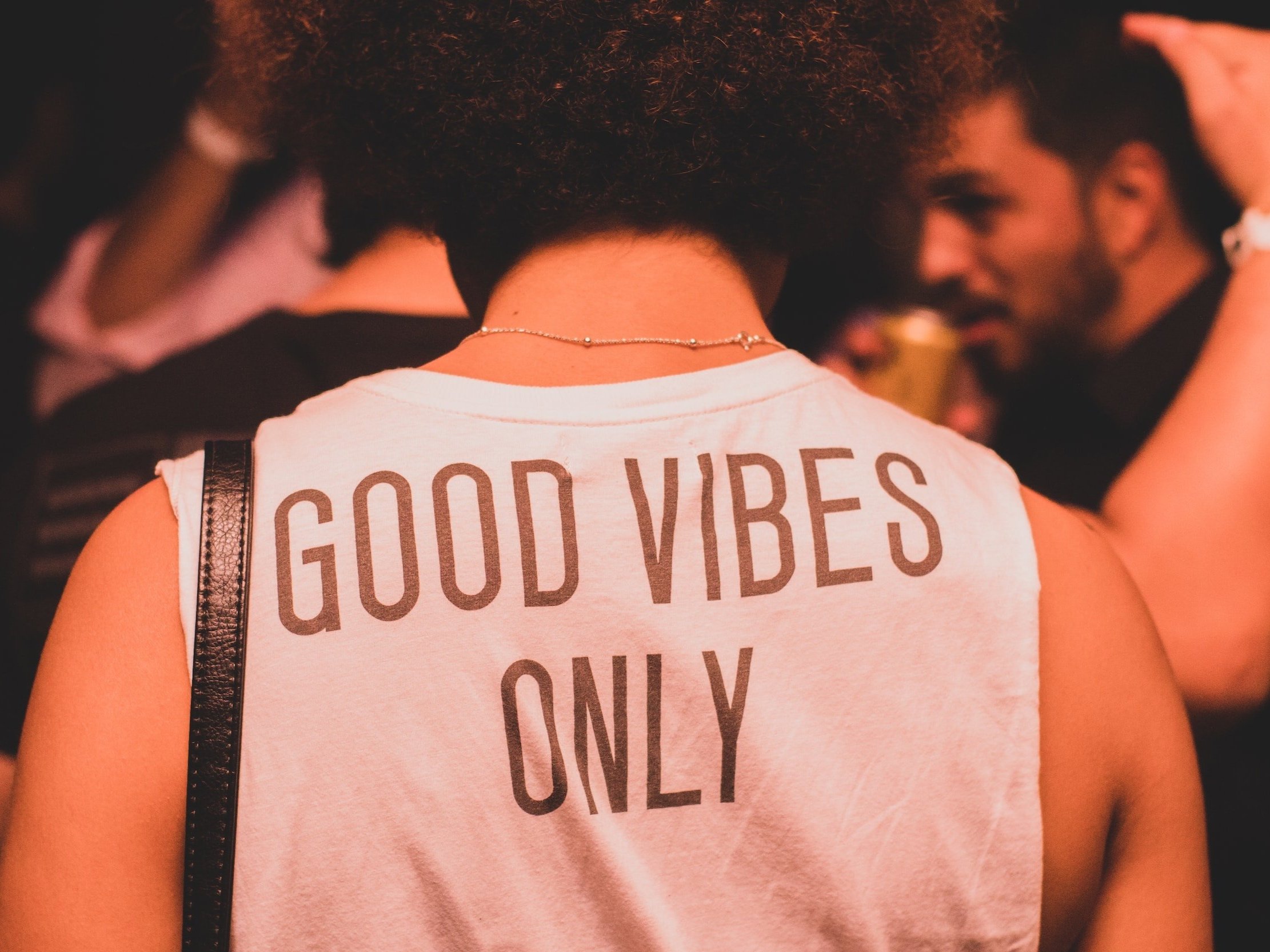 A woman with her back to us wears a t-shirt with the words "Good Vibes Only" printed on it.