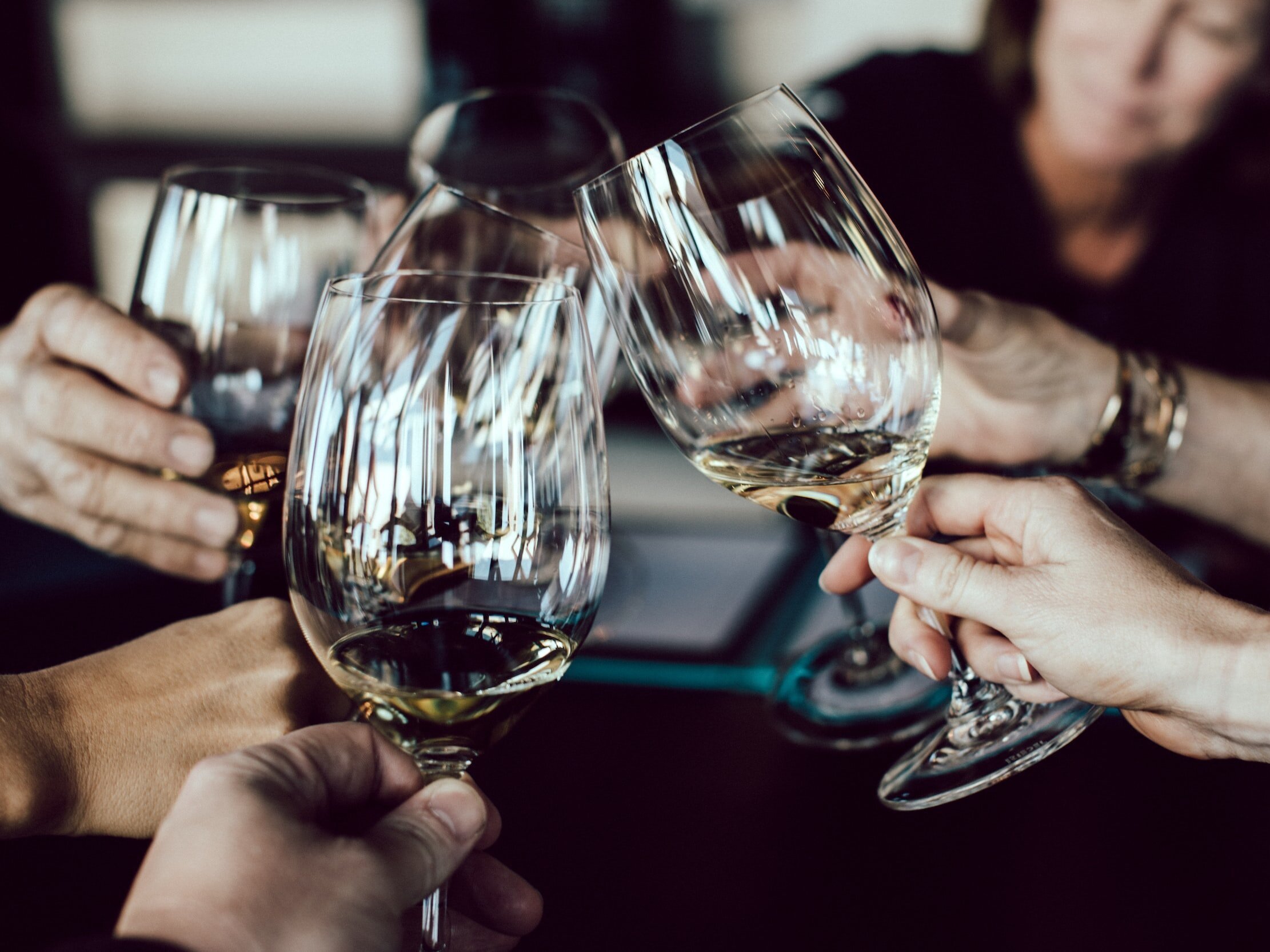 A group of people at a table are raising and clinking their wine glasses to express their appreciation.
